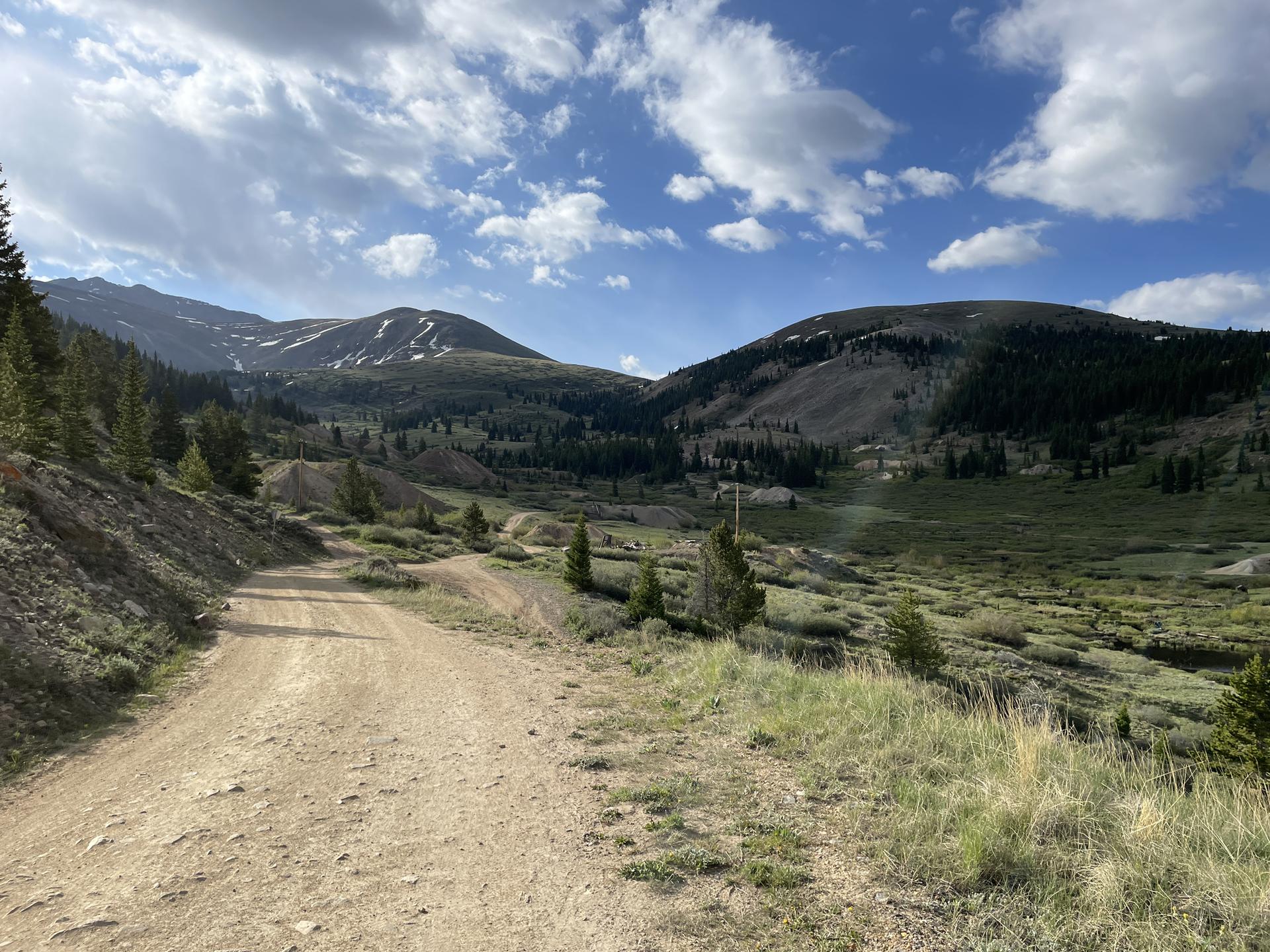 Dirt road winding through a lush green mountain valley under a blue sky.