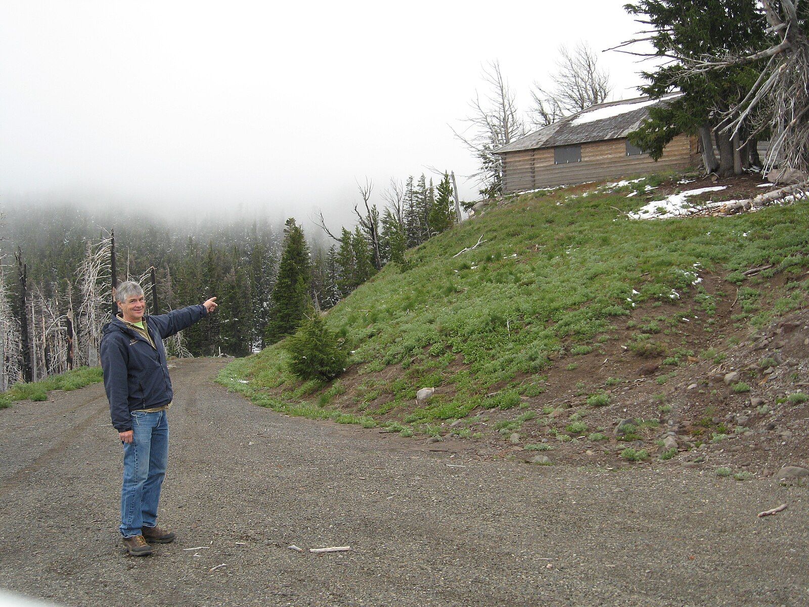 Person pointing on a gravel road towards a cabin on a foggy, forested hill. - Wagon Road and Tilly Jane Trail Loop