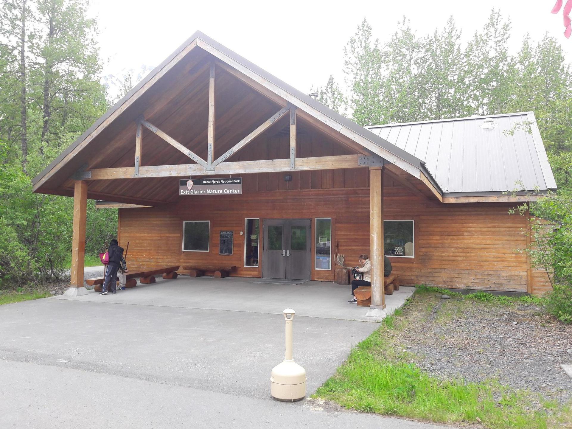 A wooden building with a large porch and people at the entrance.