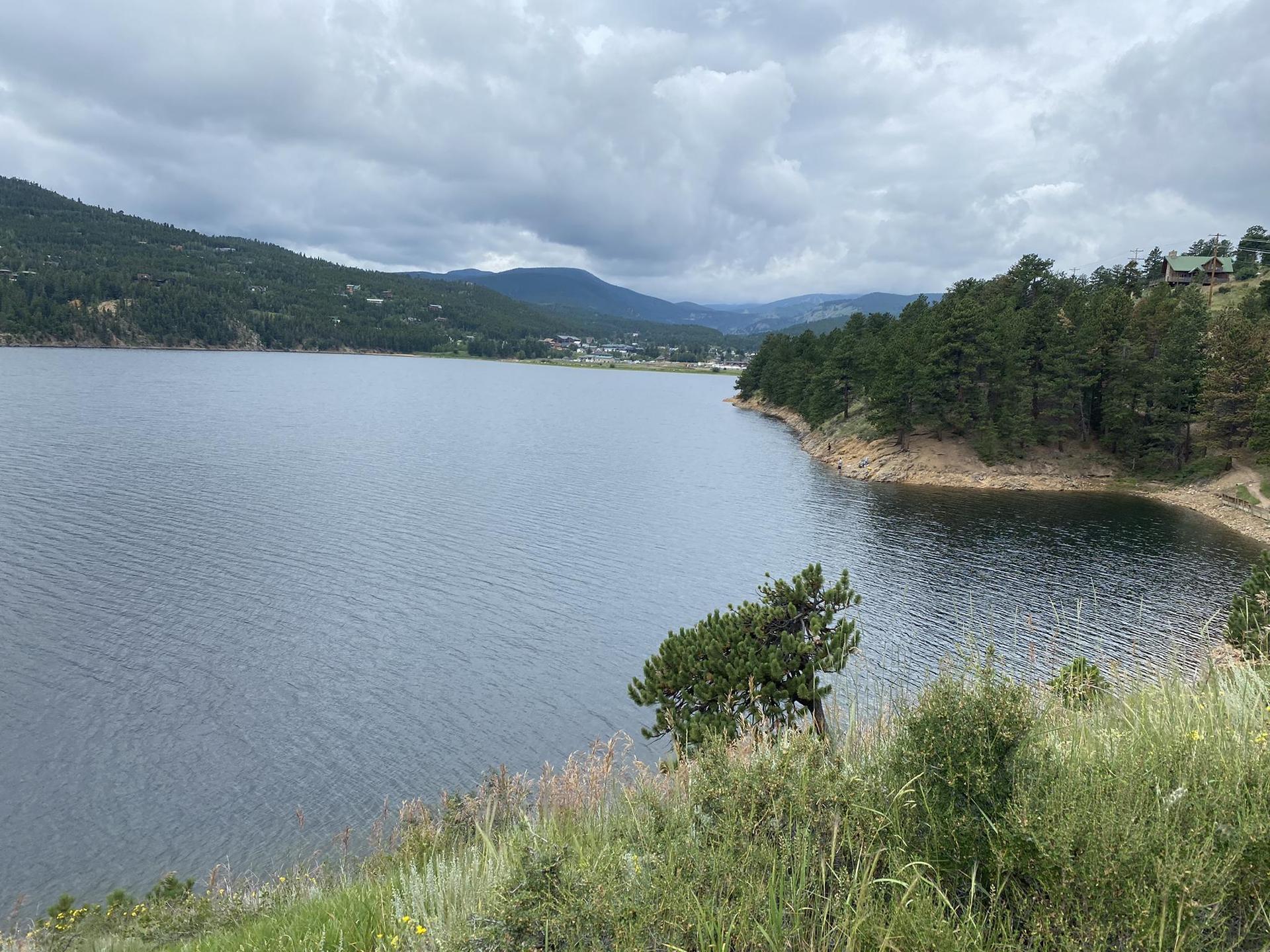 A wide lake with forested shores under a cloudy, expansive sky.
