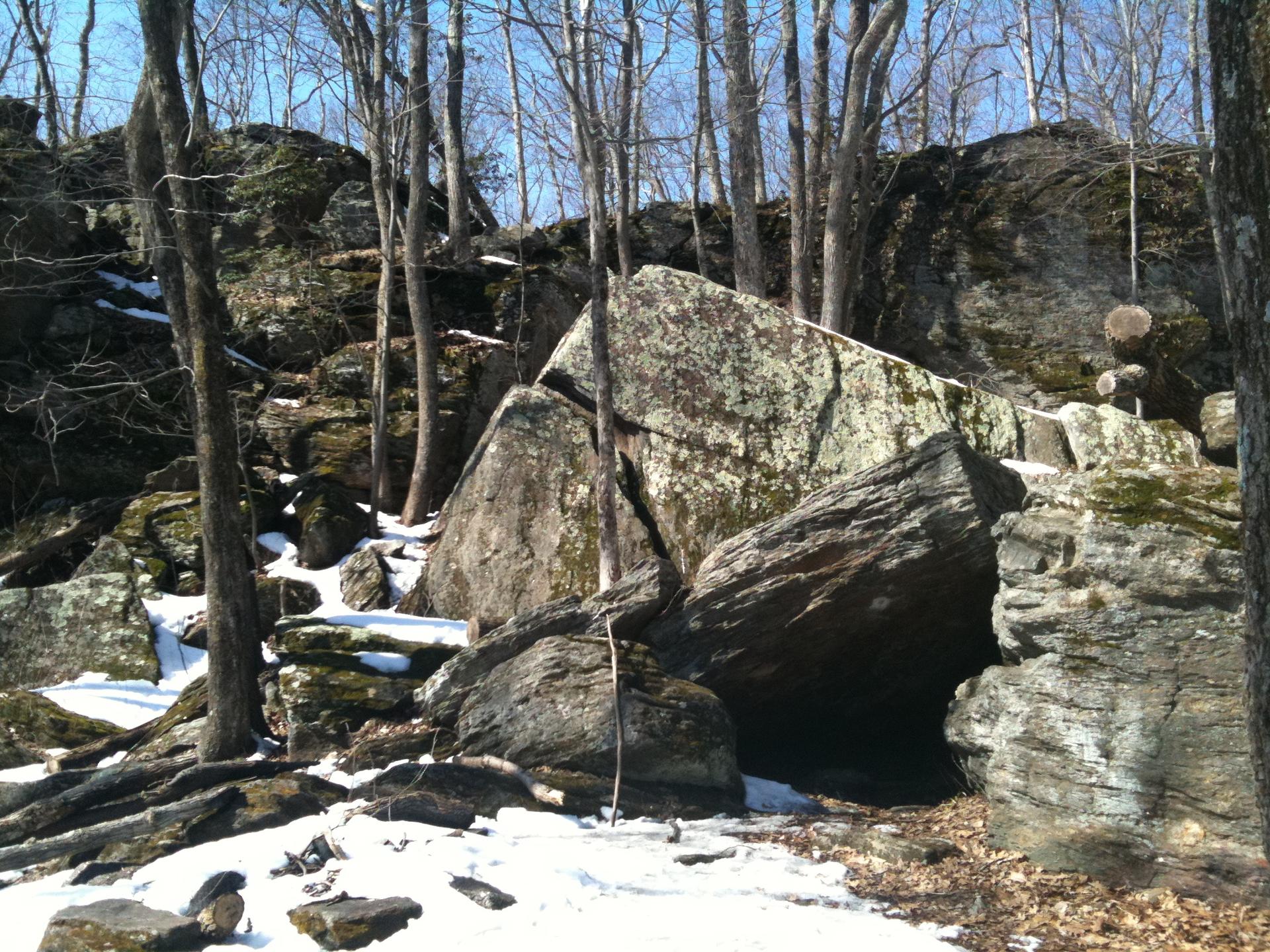 Sunny forest scene with massive boulders and patches of melting snow.