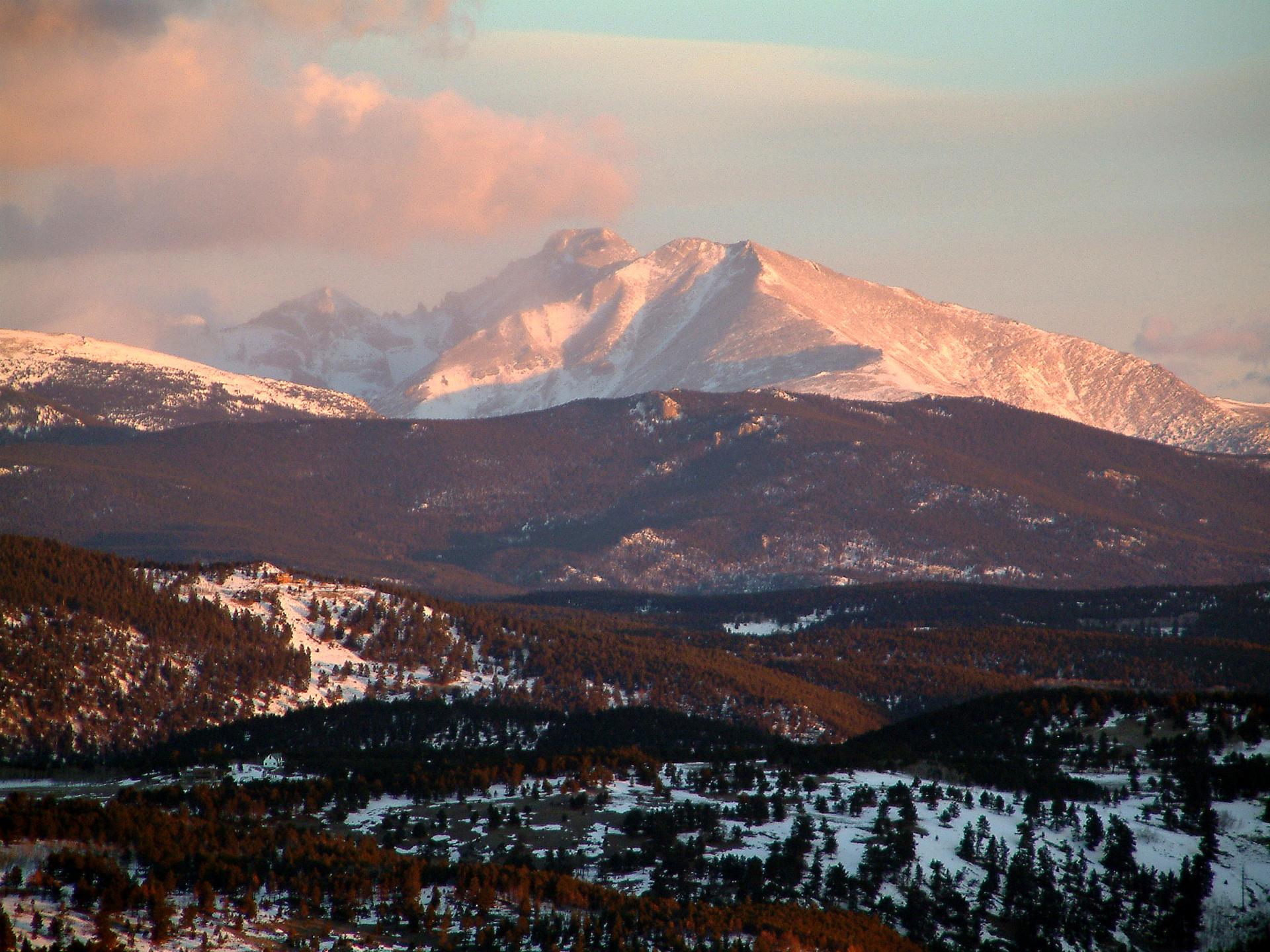 Majestic snowy mountains and forested hills at sunset with pink clouds.