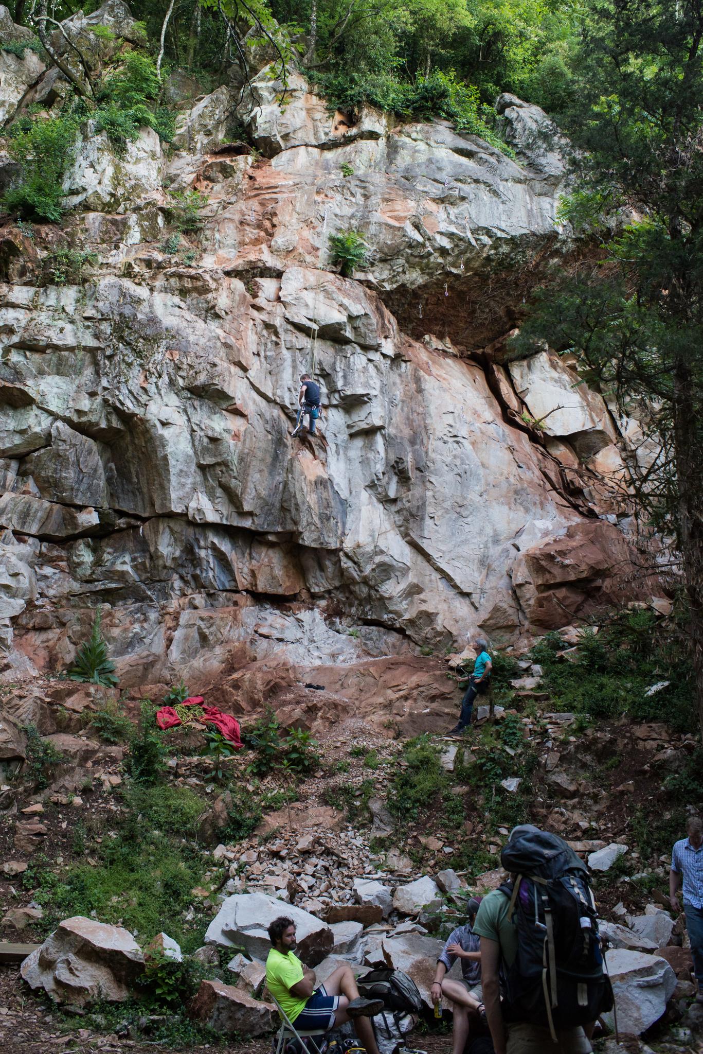 People rock climbing on a tall, rugged cliff face with others below.