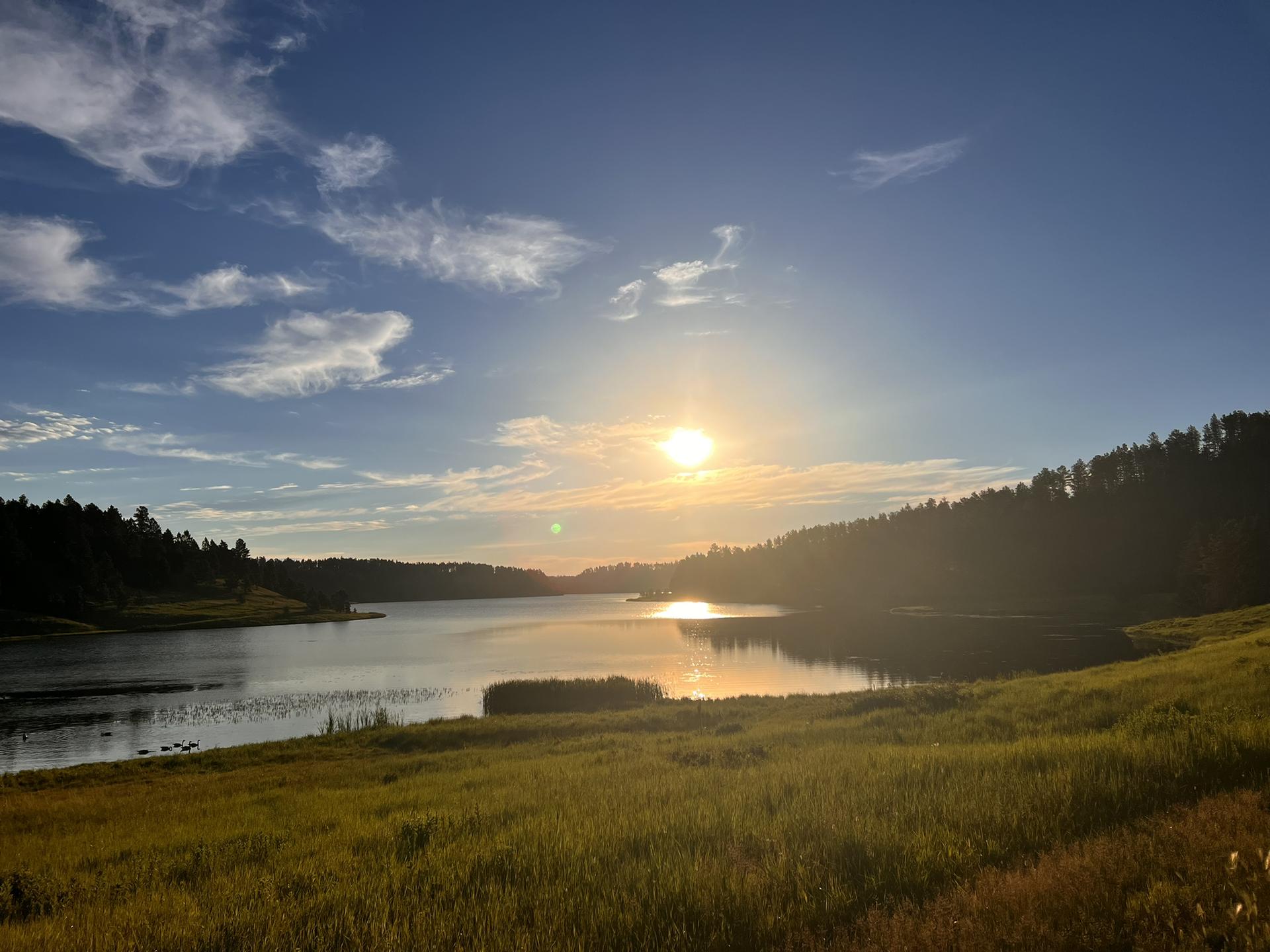 Golden sunset over a calm lake surrounded by dark forested hills.