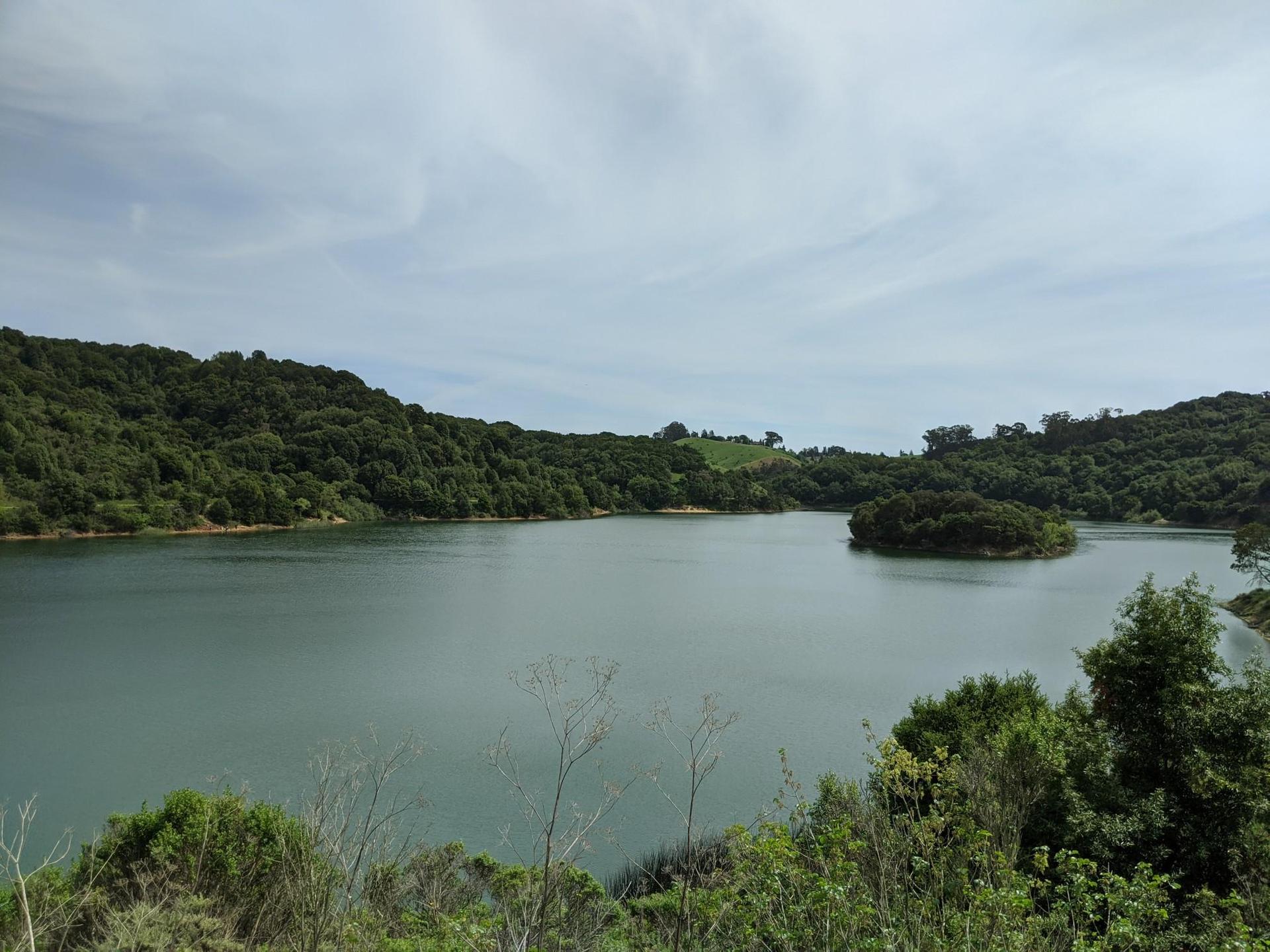 Wide view of a calm lake with a small island and forested hills.