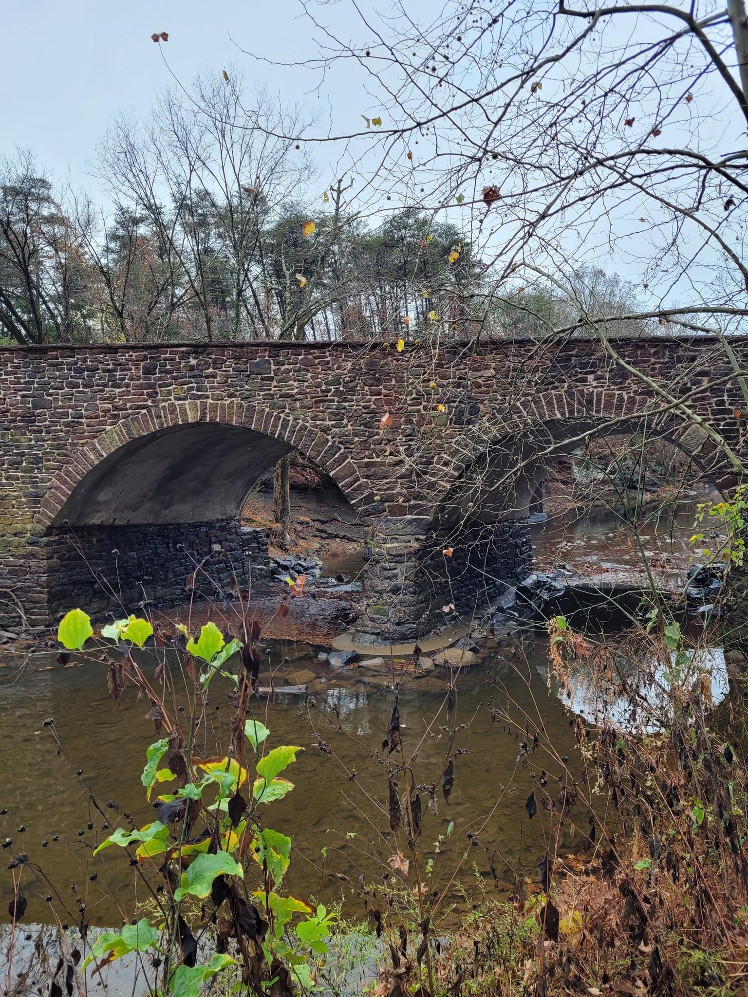 Stone arch bridge over a stream, surrounded by autumn foliage.