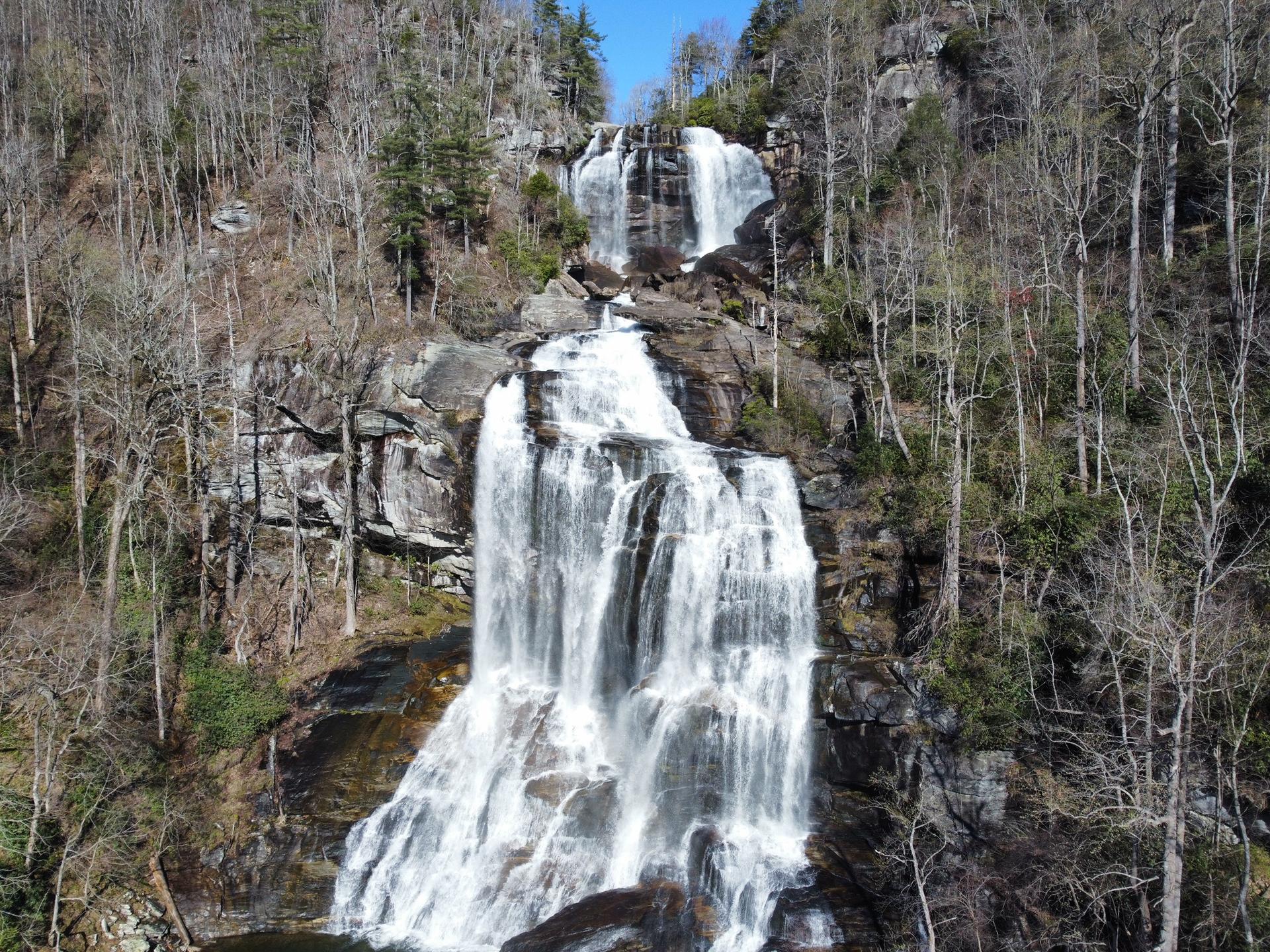 Majestic multi-tiered waterfall flowing over rocks, surrounded by mostly bare trees.
