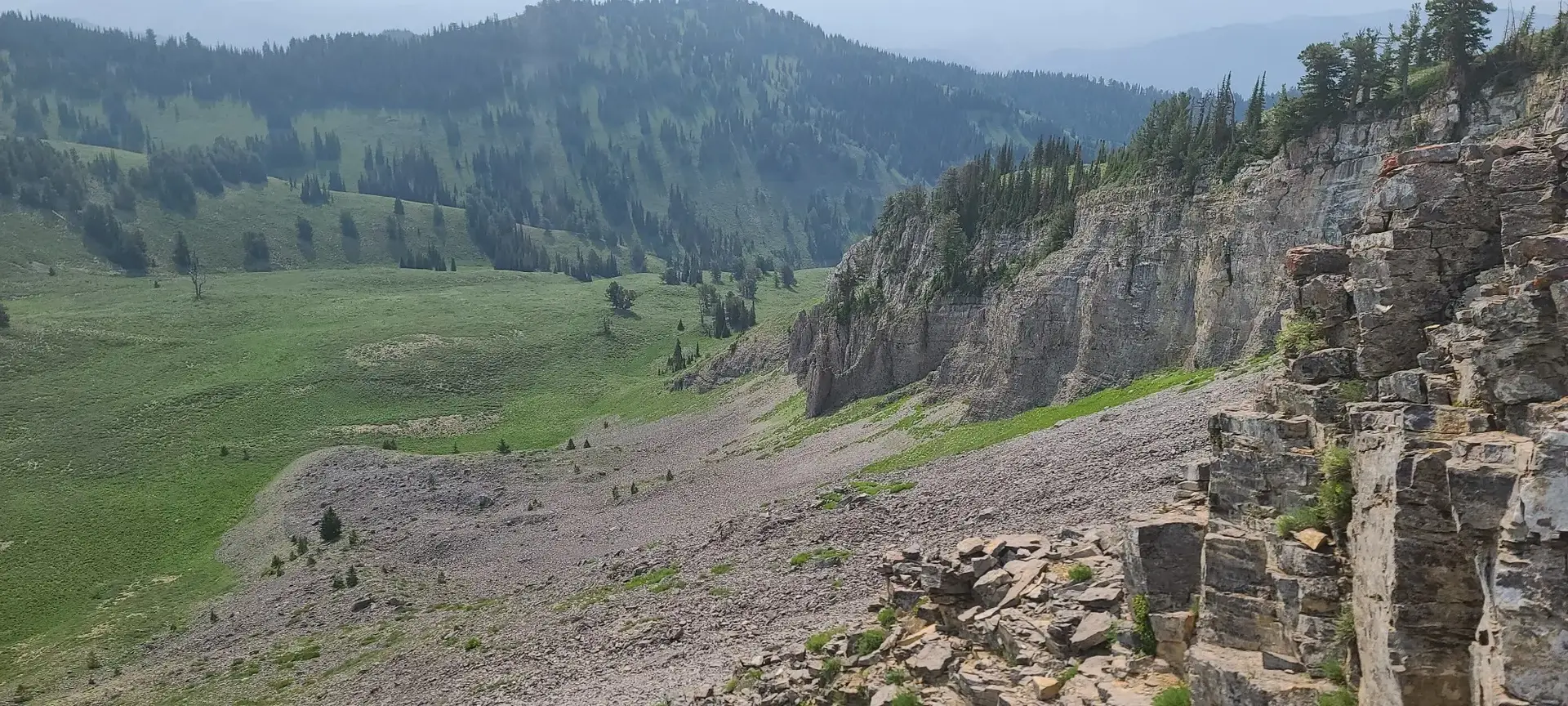Vast mountain valley with steep rocky cliffs and a green meadow below.