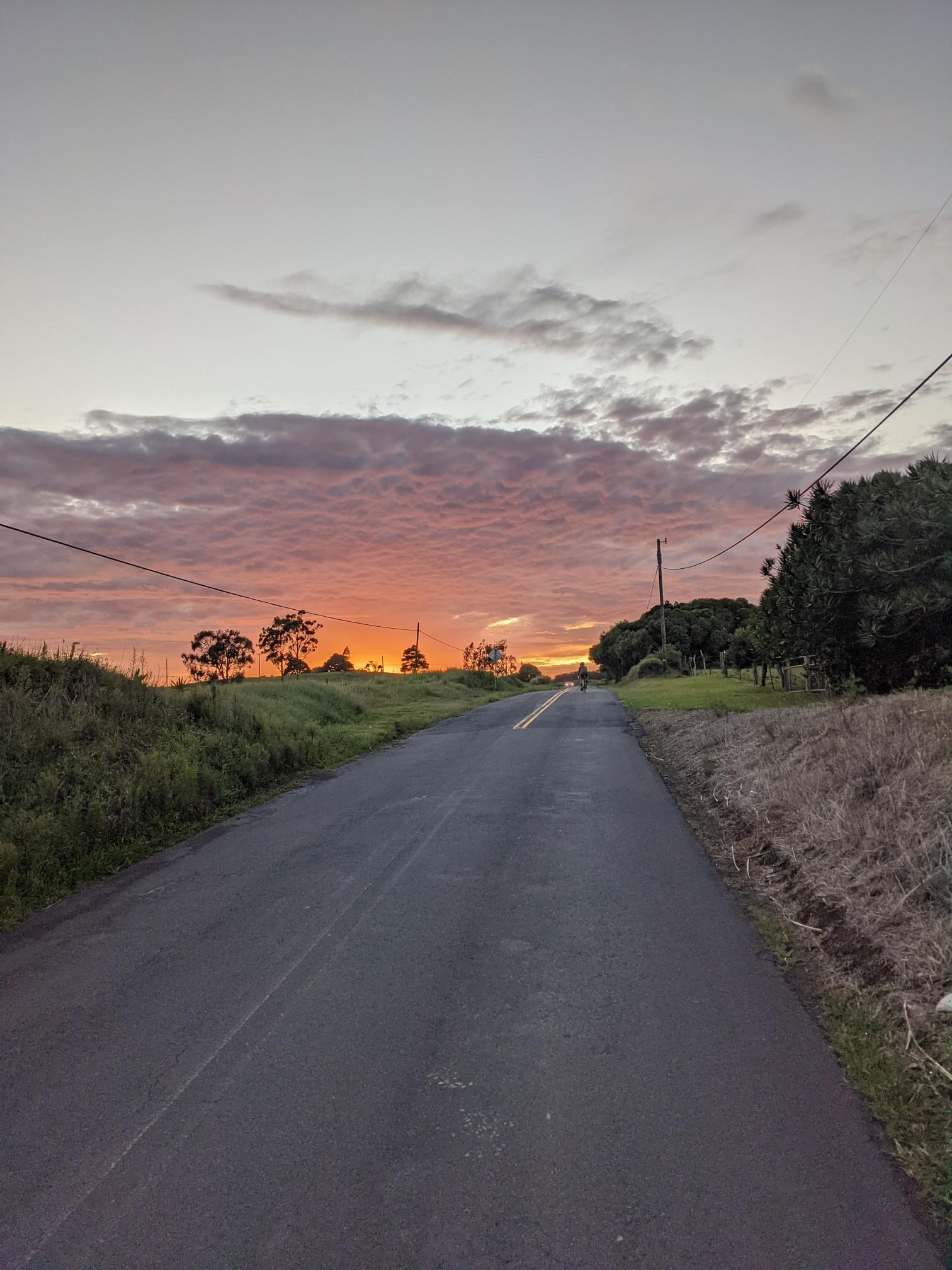 Empty paved road leading towards a vibrant orange and pink sunset.