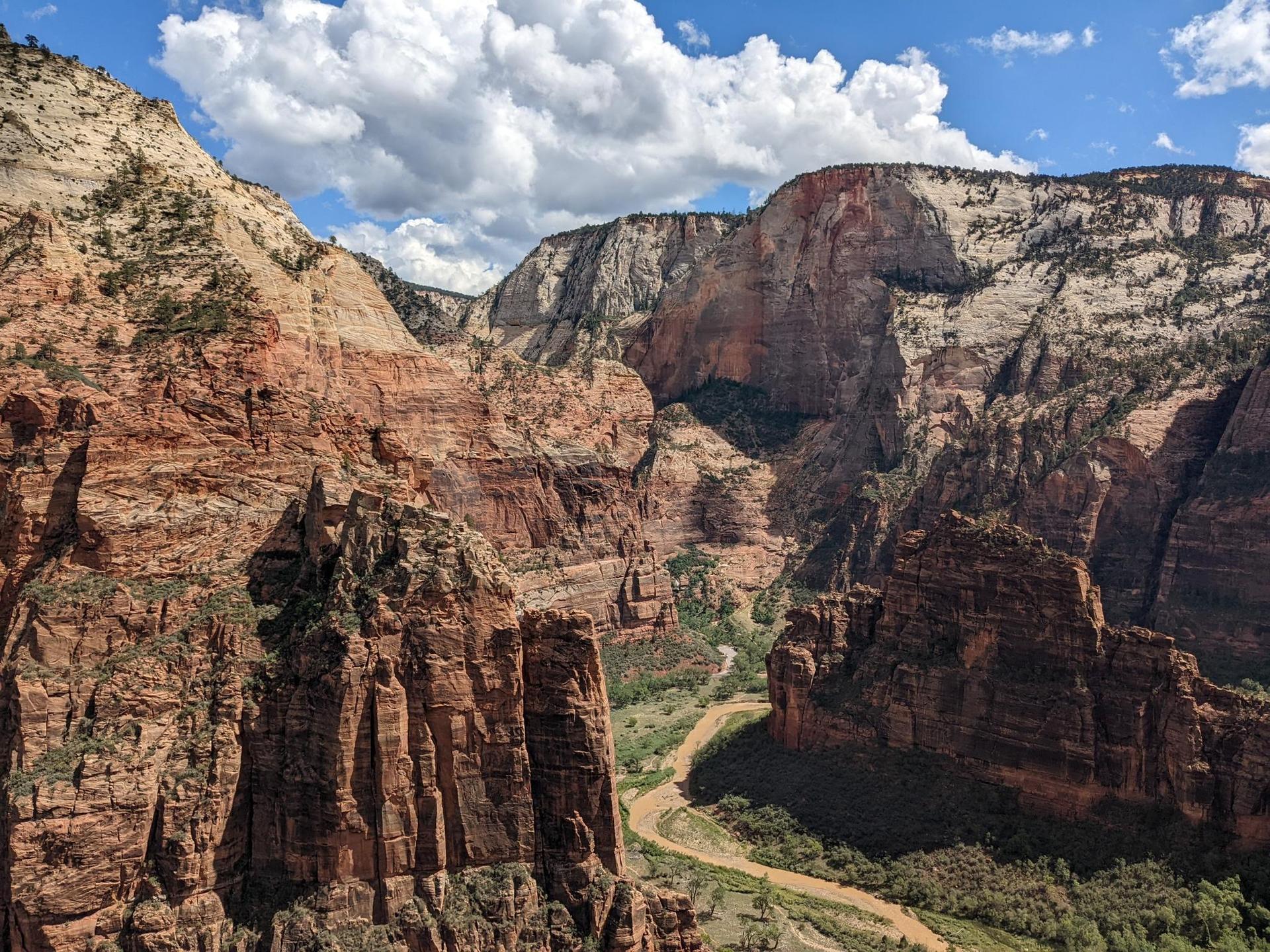 Vast canyon landscape with towering red cliffs, a winding river, and cloudy sky.