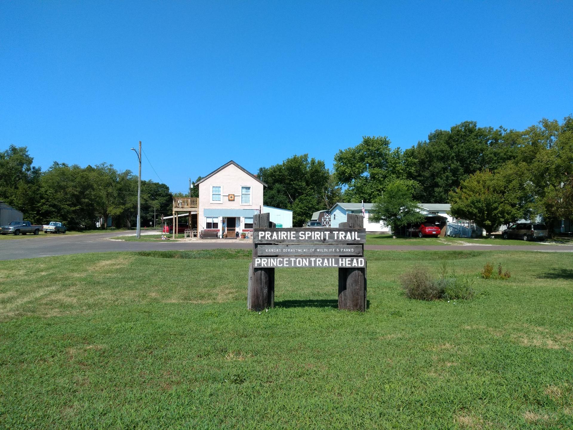 A wooden sign in a grassy field with distant buildings under a clear sky.