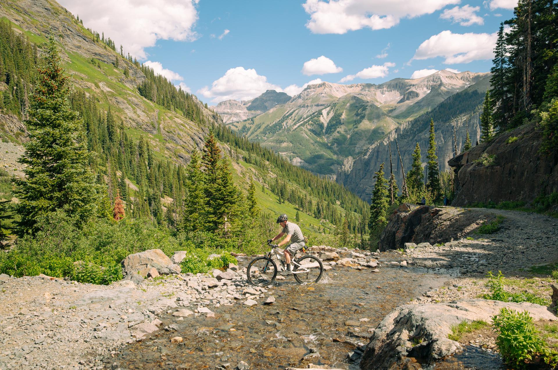 Mountain biker crossing a rocky stream on a sunny day.