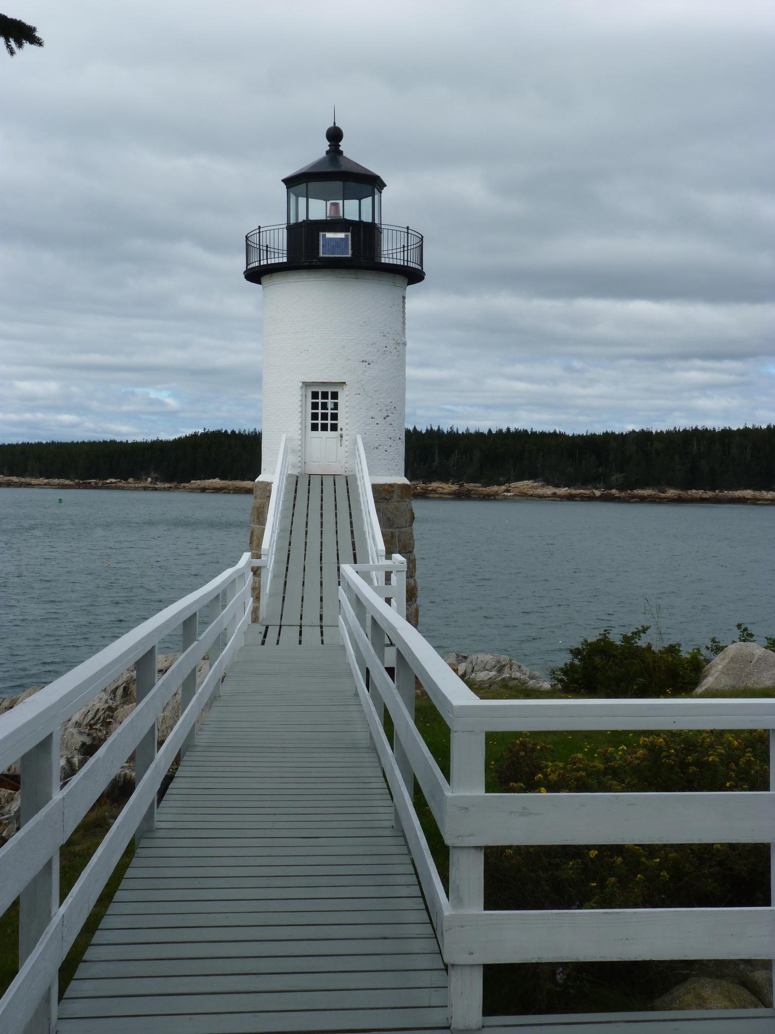 A white lighthouse with a long wooden walkway under an overcast sky.