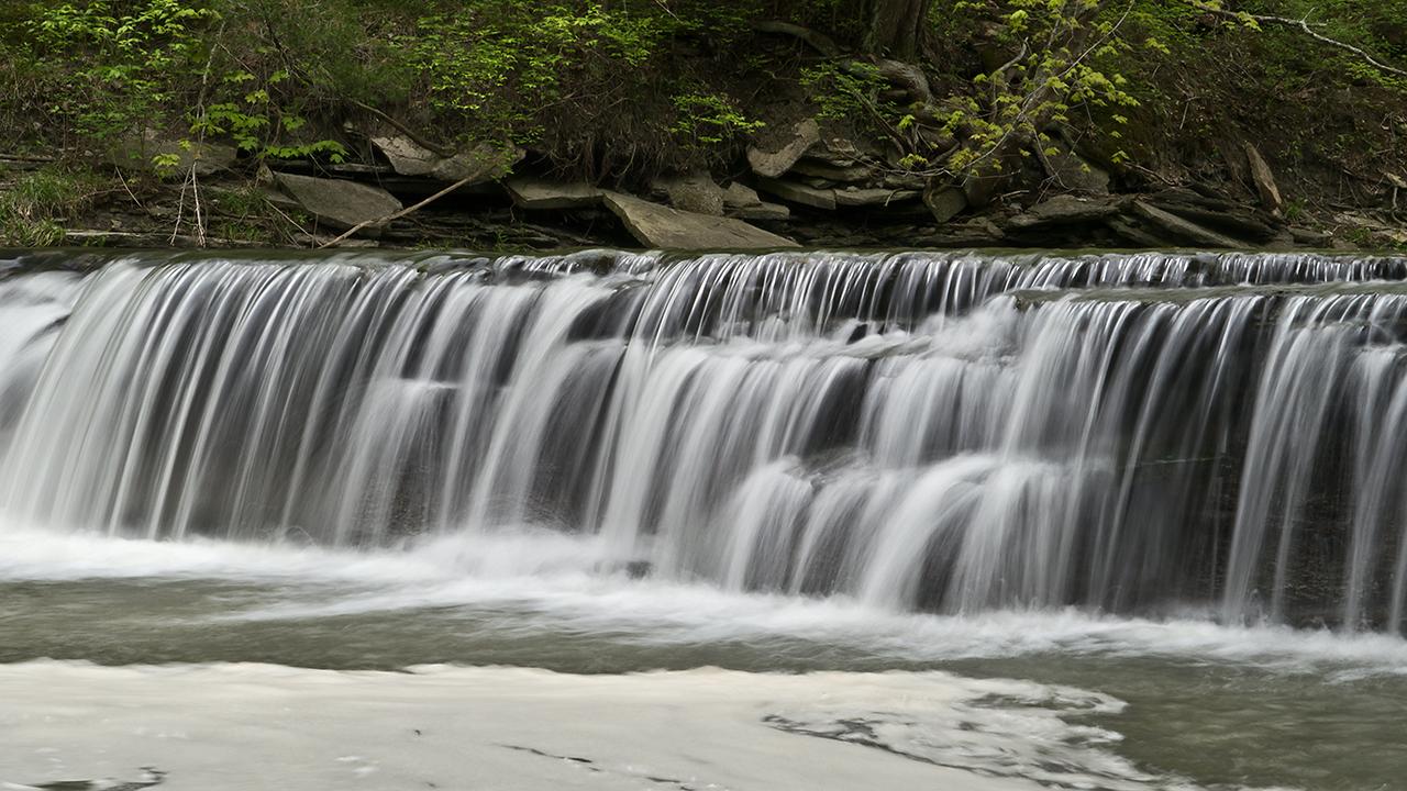 Wide, multi-tiered waterfall with lush green foliage above, soft light.