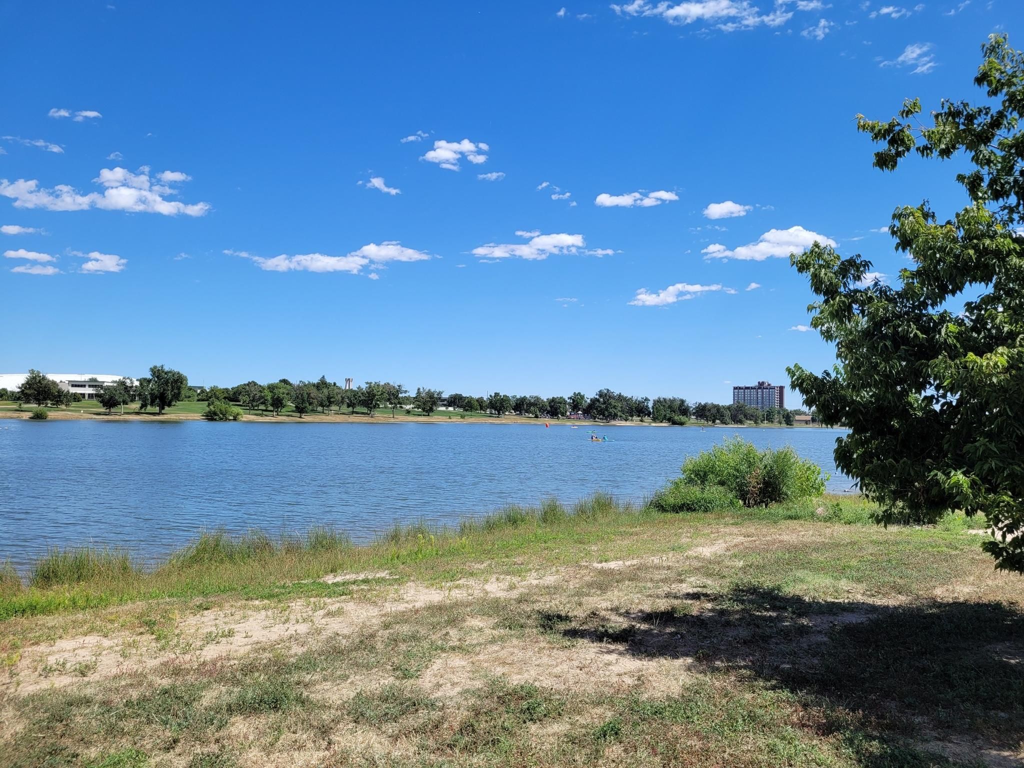 Wide lake under a bright blue sky with distant buildings and trees. - Prospect Lake Fitness Trail