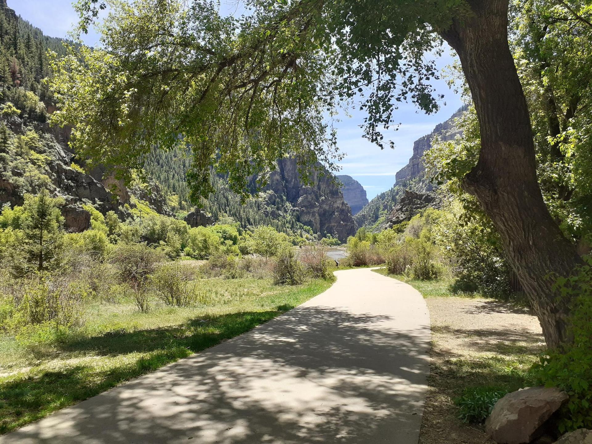 Paved path through a green valley, framed by trees, leading into a canyon.