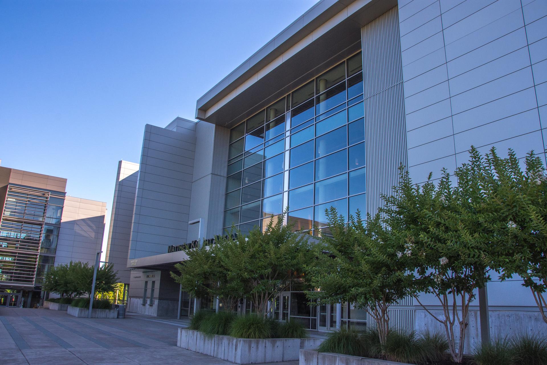 Modern building with large glass windows and trees under a clear blue sky.