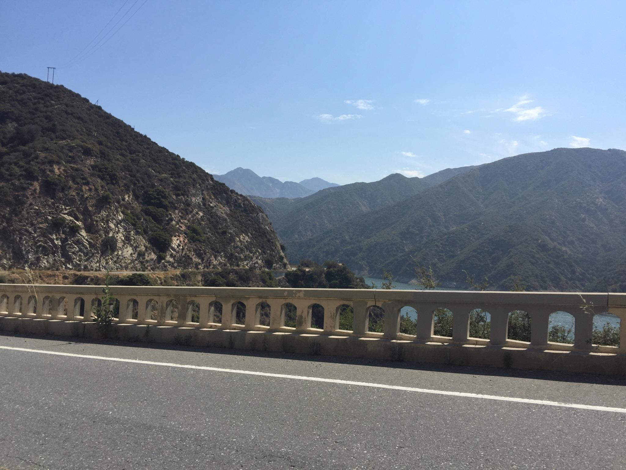 Paved road with a concrete barrier overlooking a vast mountain valley.