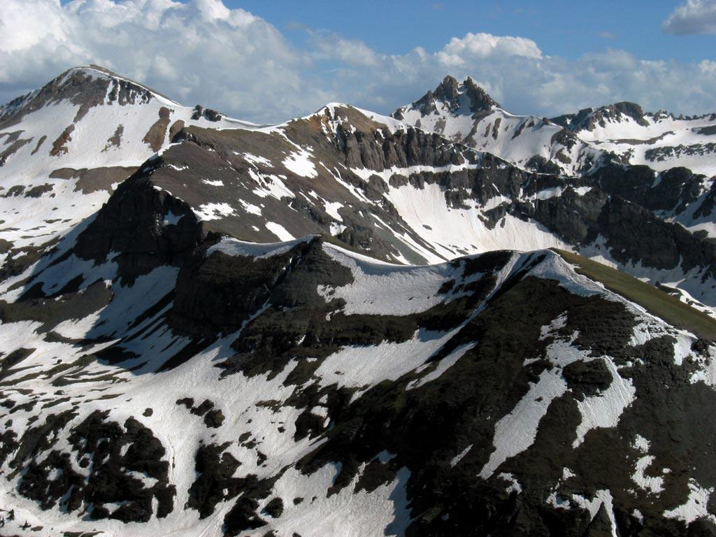 Snow-capped rugged mountains with dark rock under a bright, cloudy sky.