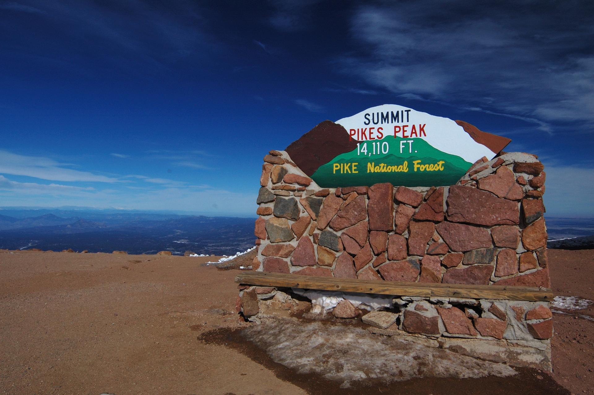 Stone monument with a sign on a barren mountain top under blue sky.
