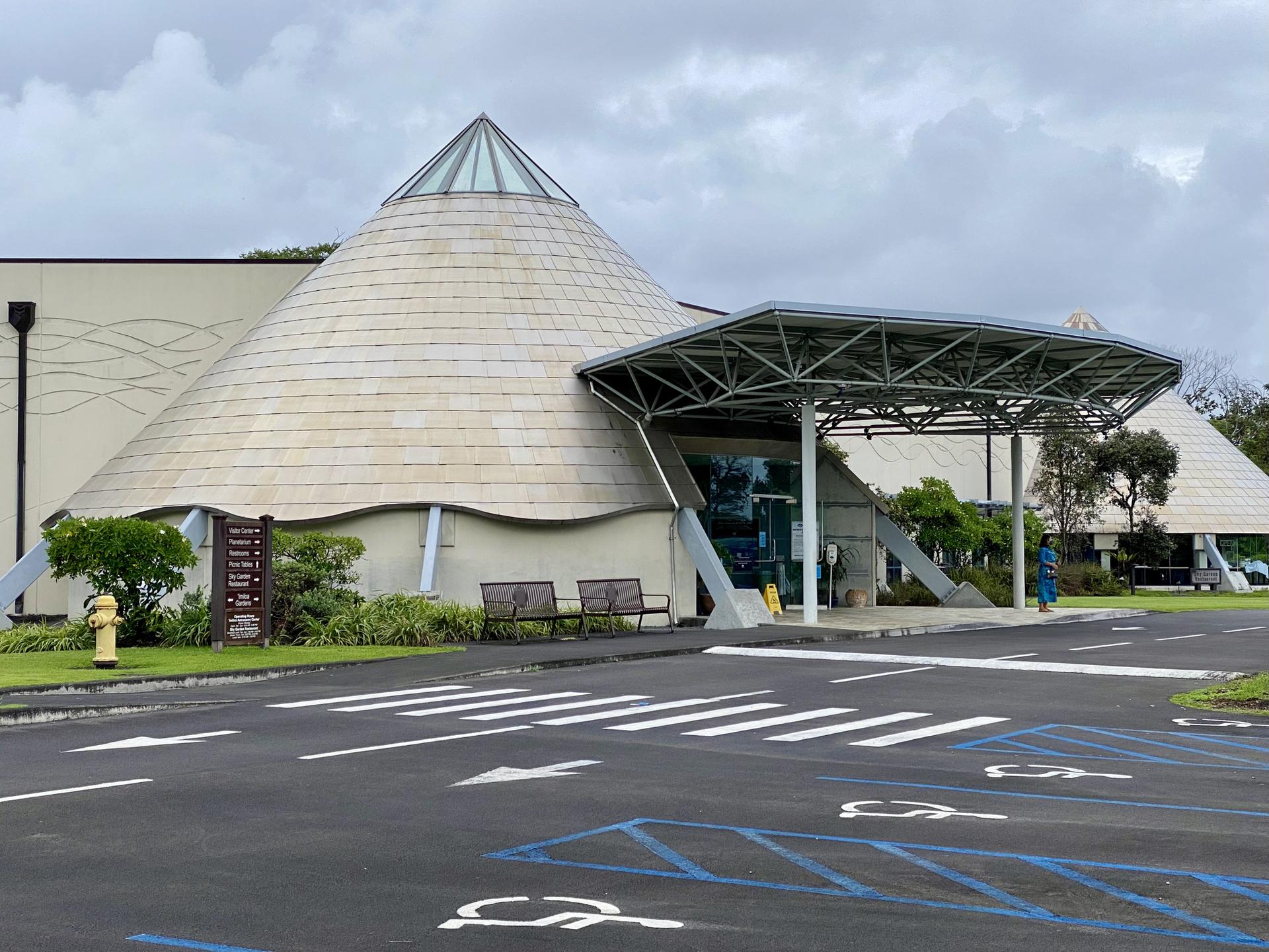Modern building with conical roof and covered entrance under an overcast sky.