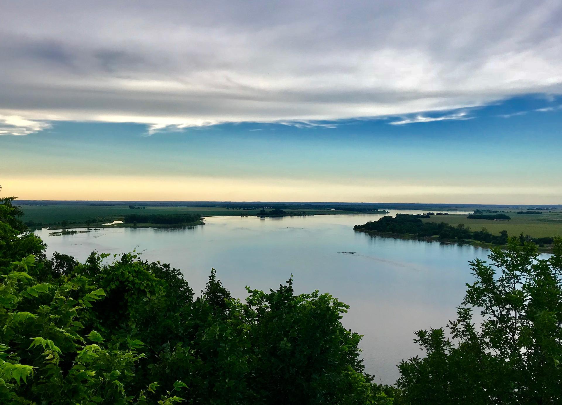 Vast body of water surrounded by green land under a dramatic, cloudy sky.