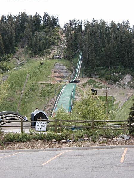 A large ski jump structure descends a steep, forested green hillside.