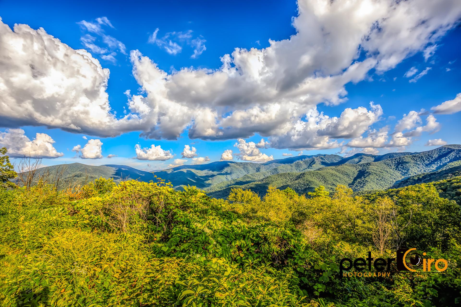 Rolling green mountains under a dramatic blue sky with large white clouds.