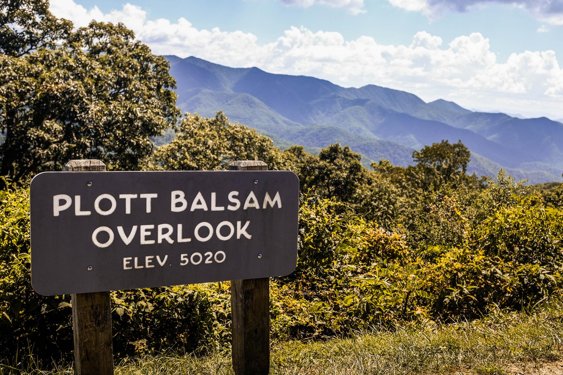 A dark signpost in a mountain landscape under a cloudy sky.