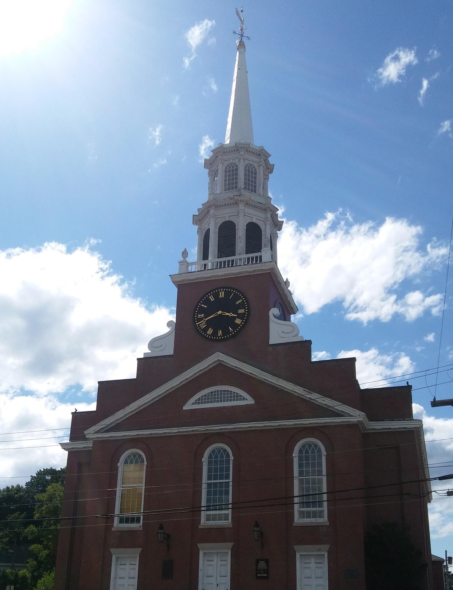 Red brick church with a tall white steeple and clock under a bright sky.