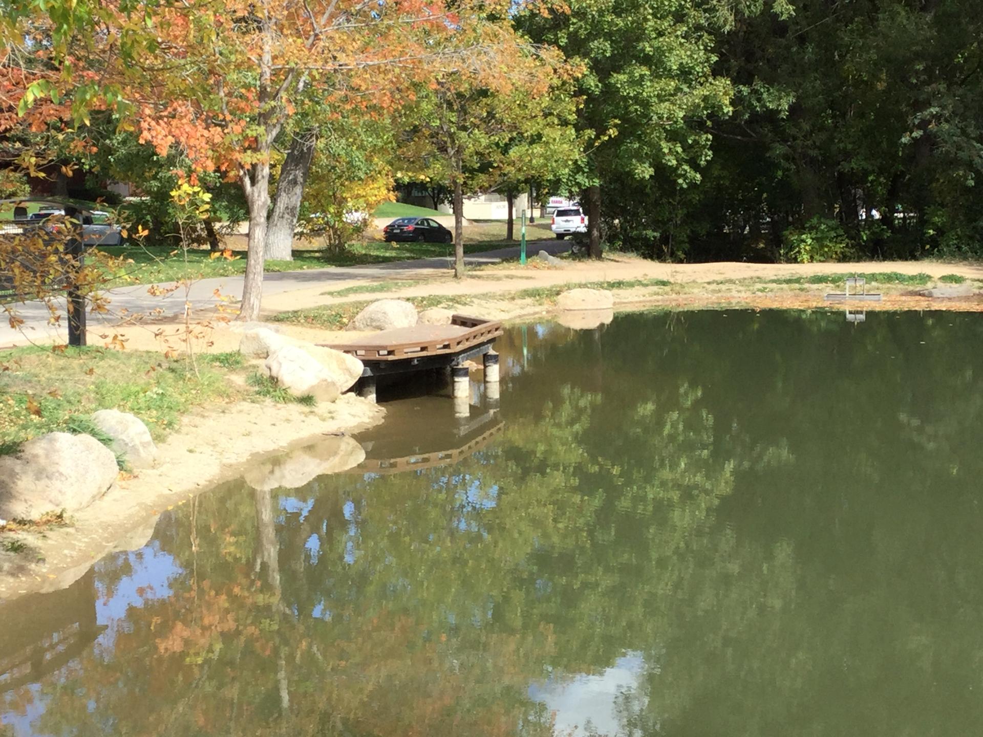 A small wooden dock extends into a calm pond surrounded by trees.