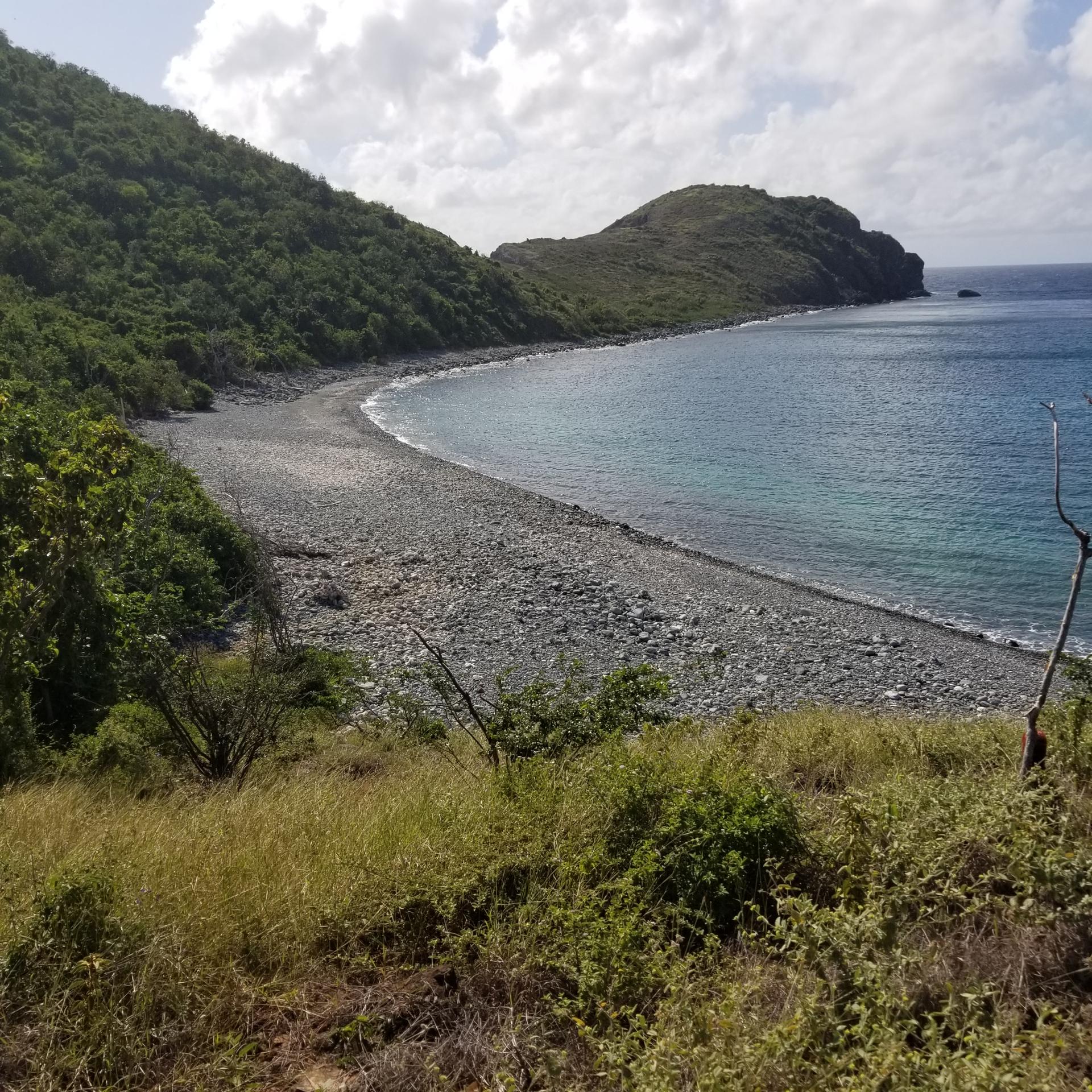 Overlook of a long, rocky beach curving into a calm blue bay.