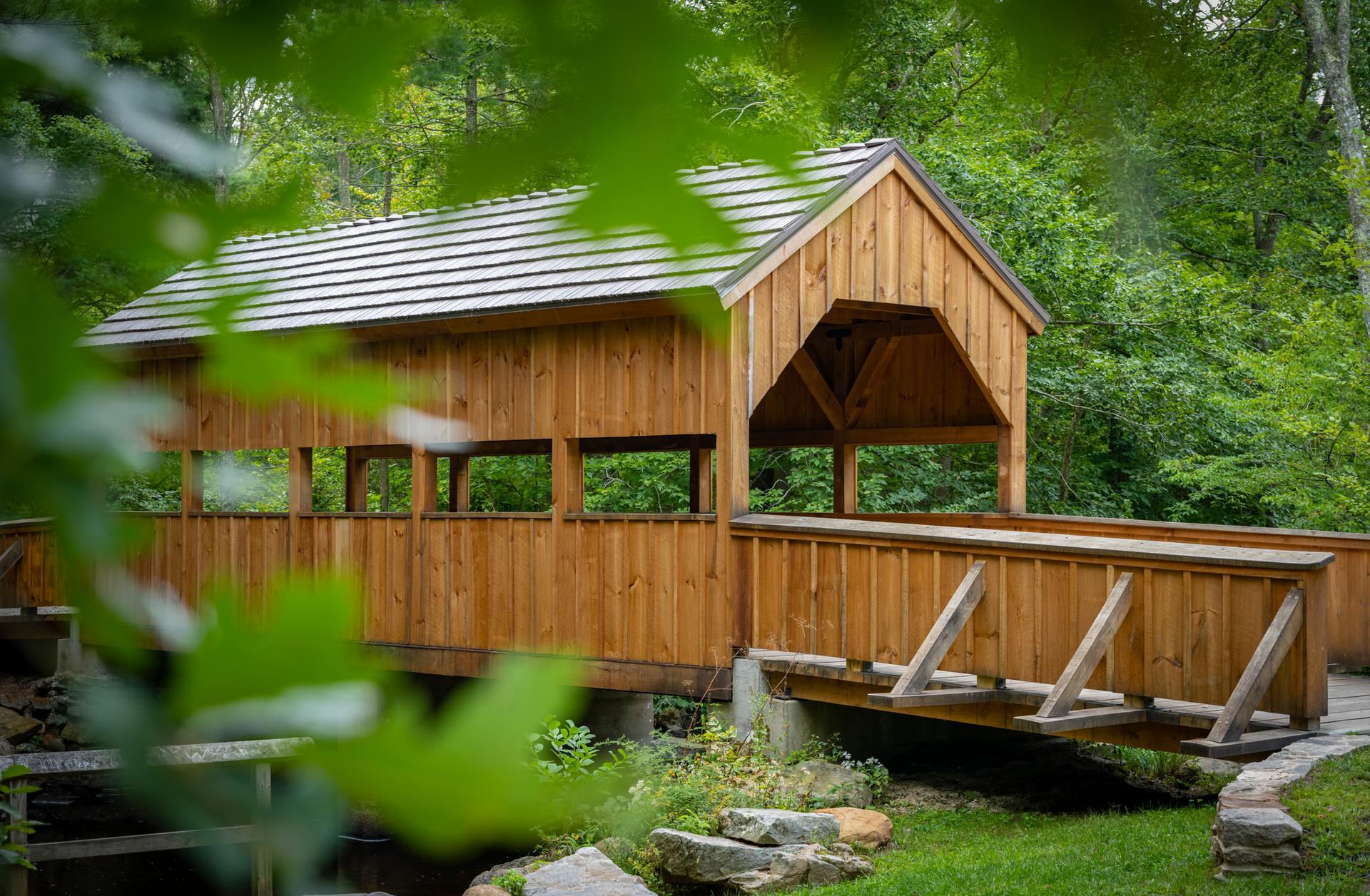 Wooden covered bridge nestled in a vibrant green forest.