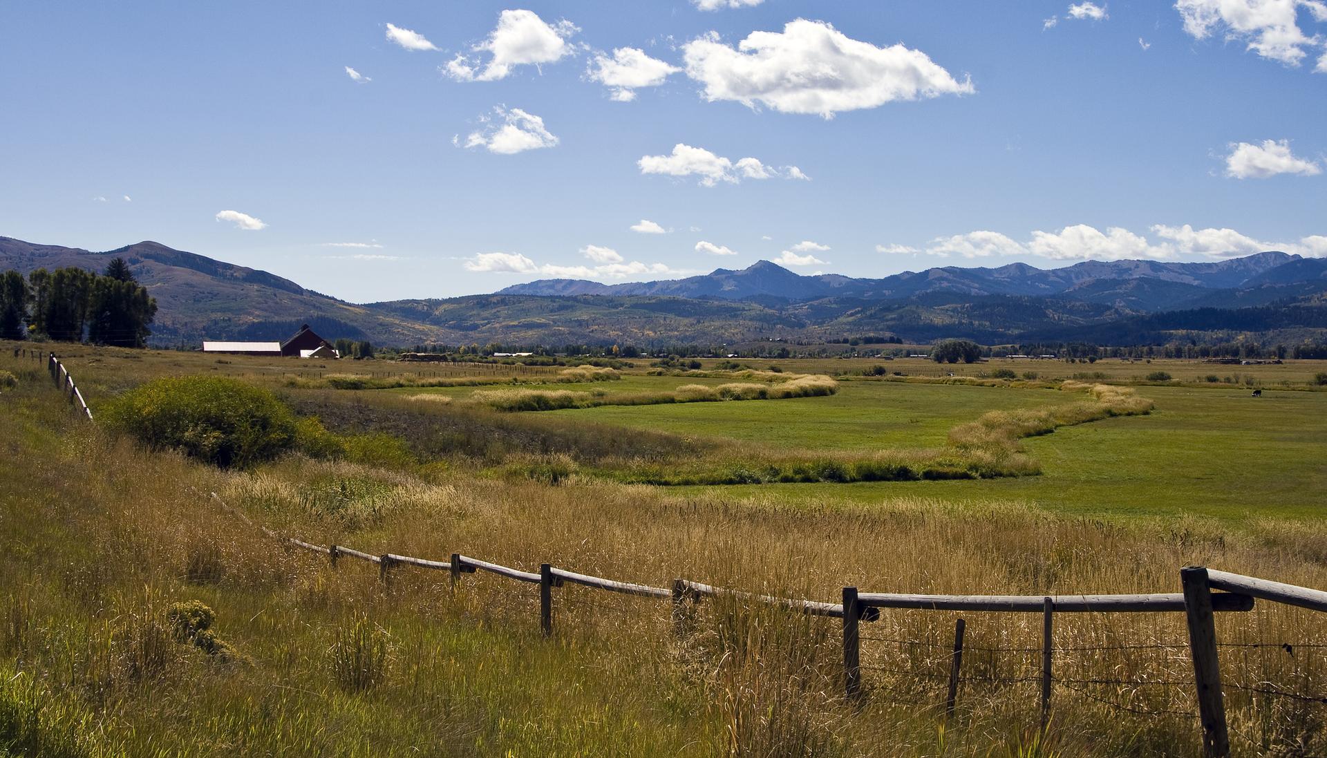 Vast green and brown fields with a fence, leading to distant mountains.