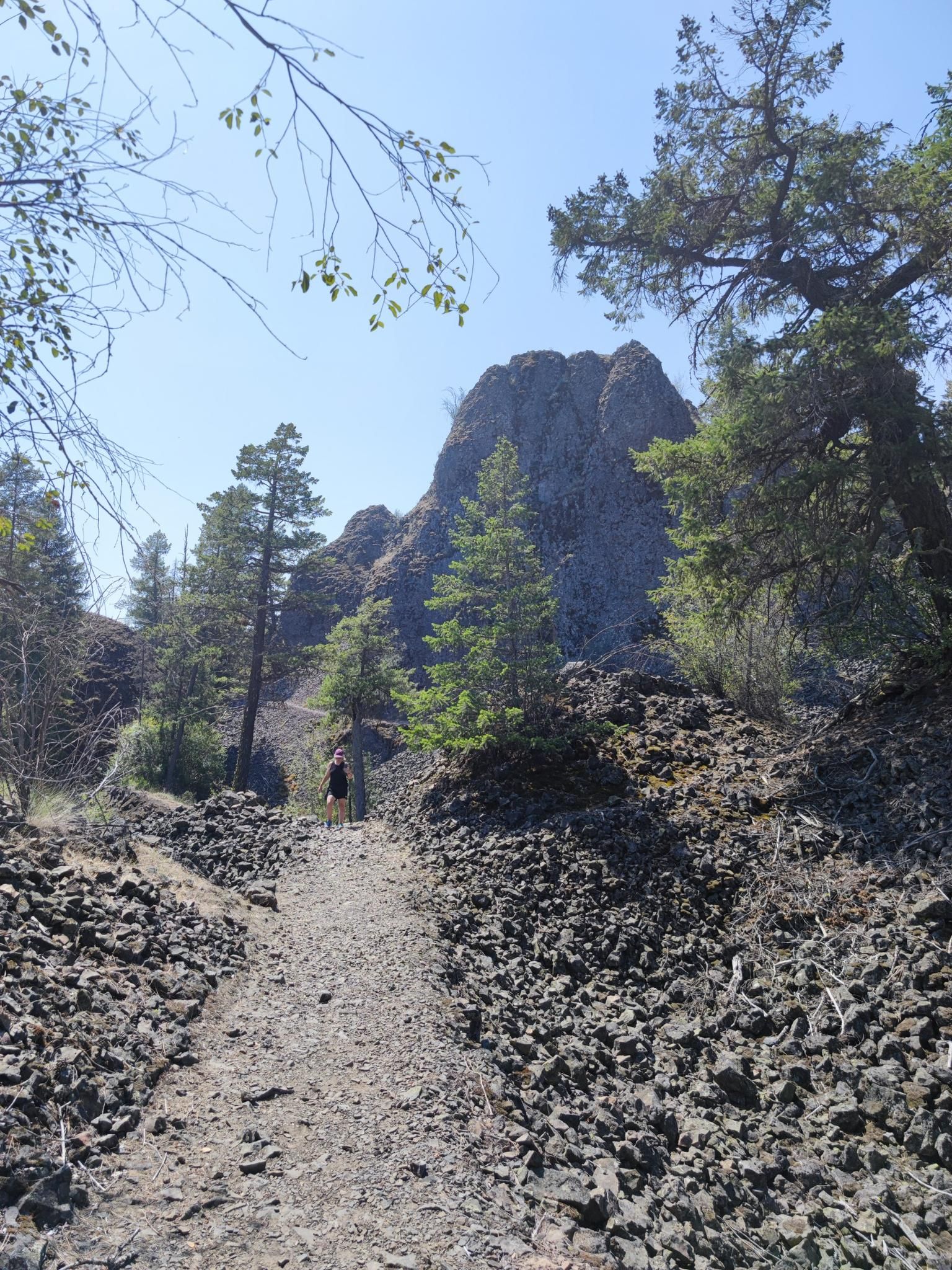 A person hikes a rocky path towards a large rock formation under a clear sky. - Pine Bluff and Trail 25 Loop
