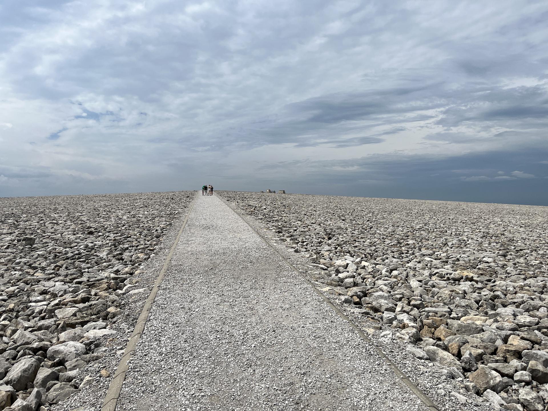 A long gravel path through a vast rocky landscape under an overcast sky, with distant people.