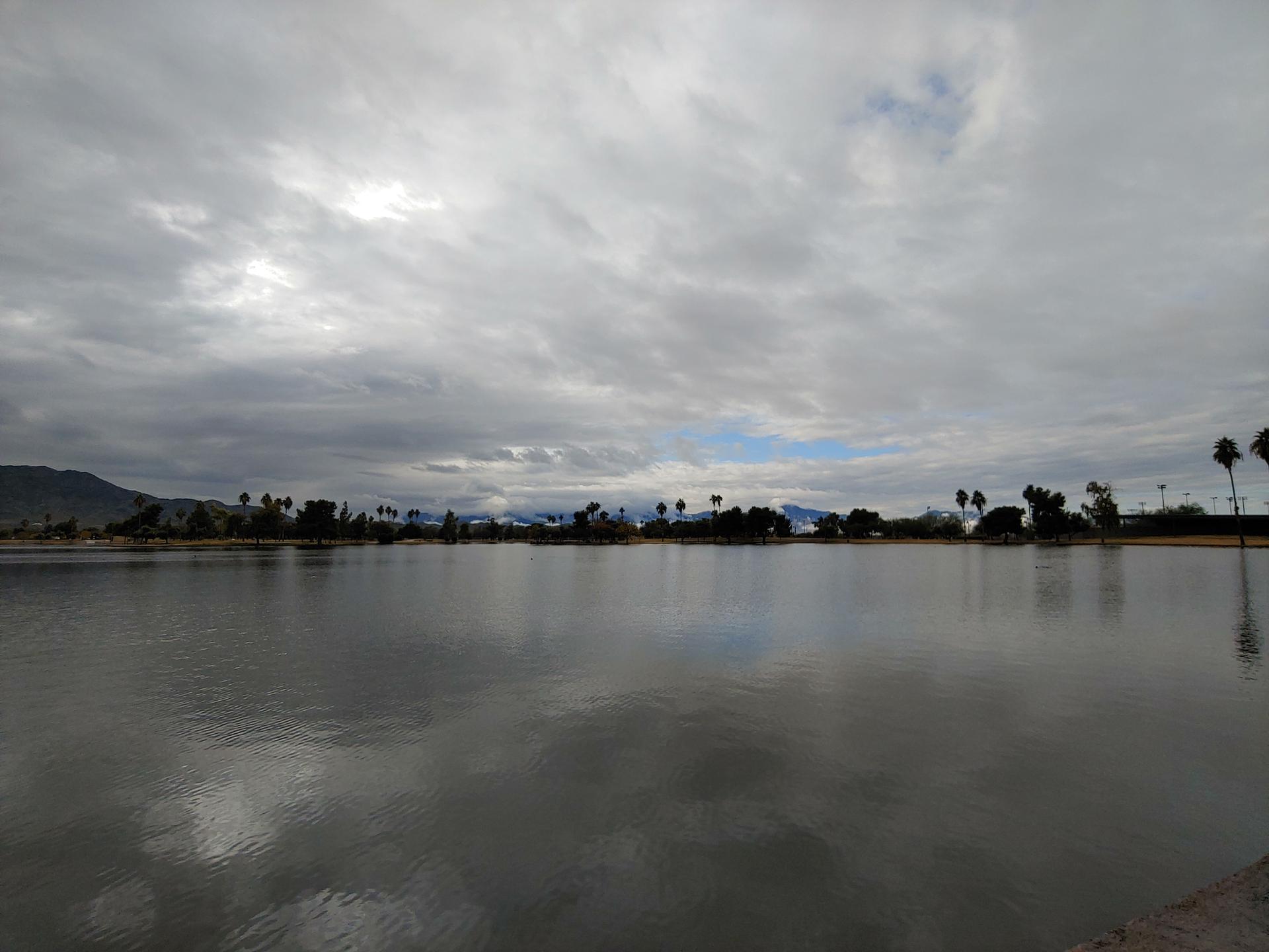 A wide lake reflecting an overcast sky with distant trees and mountains.