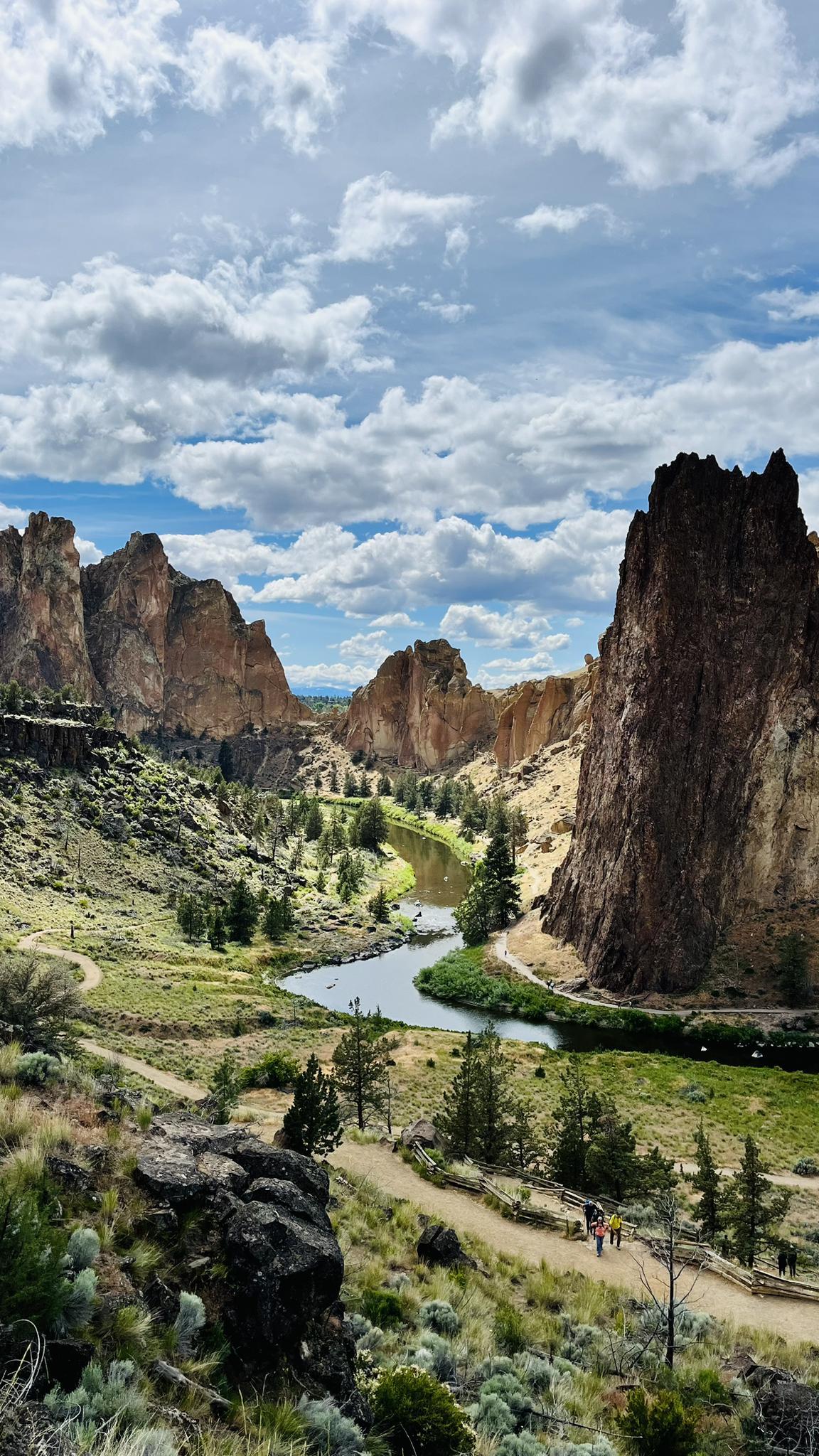 Winding river through a canyon with towering rock formations and hikers.