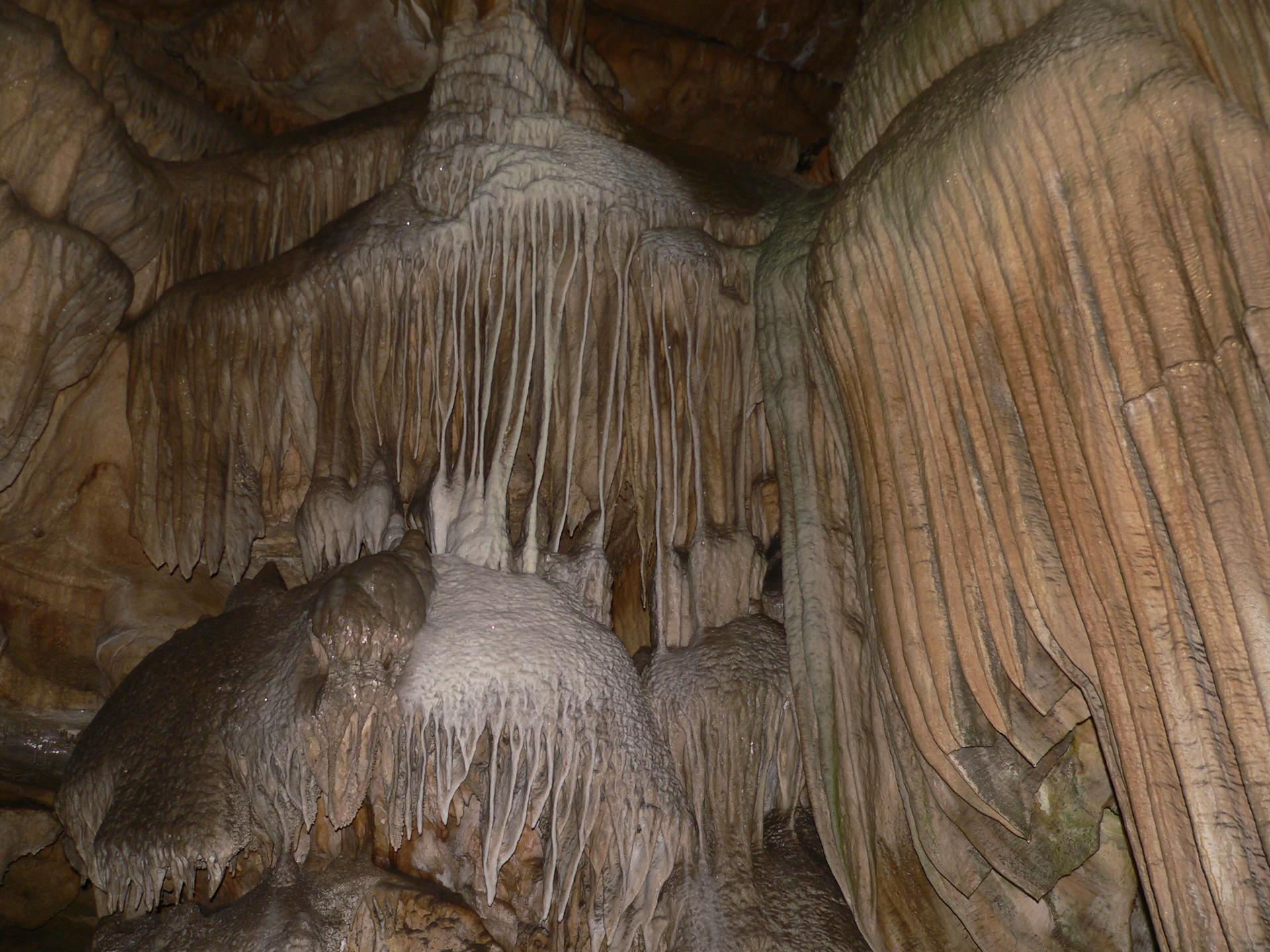 Intricate cave formations, including stalactites and flowstone, in dim light.