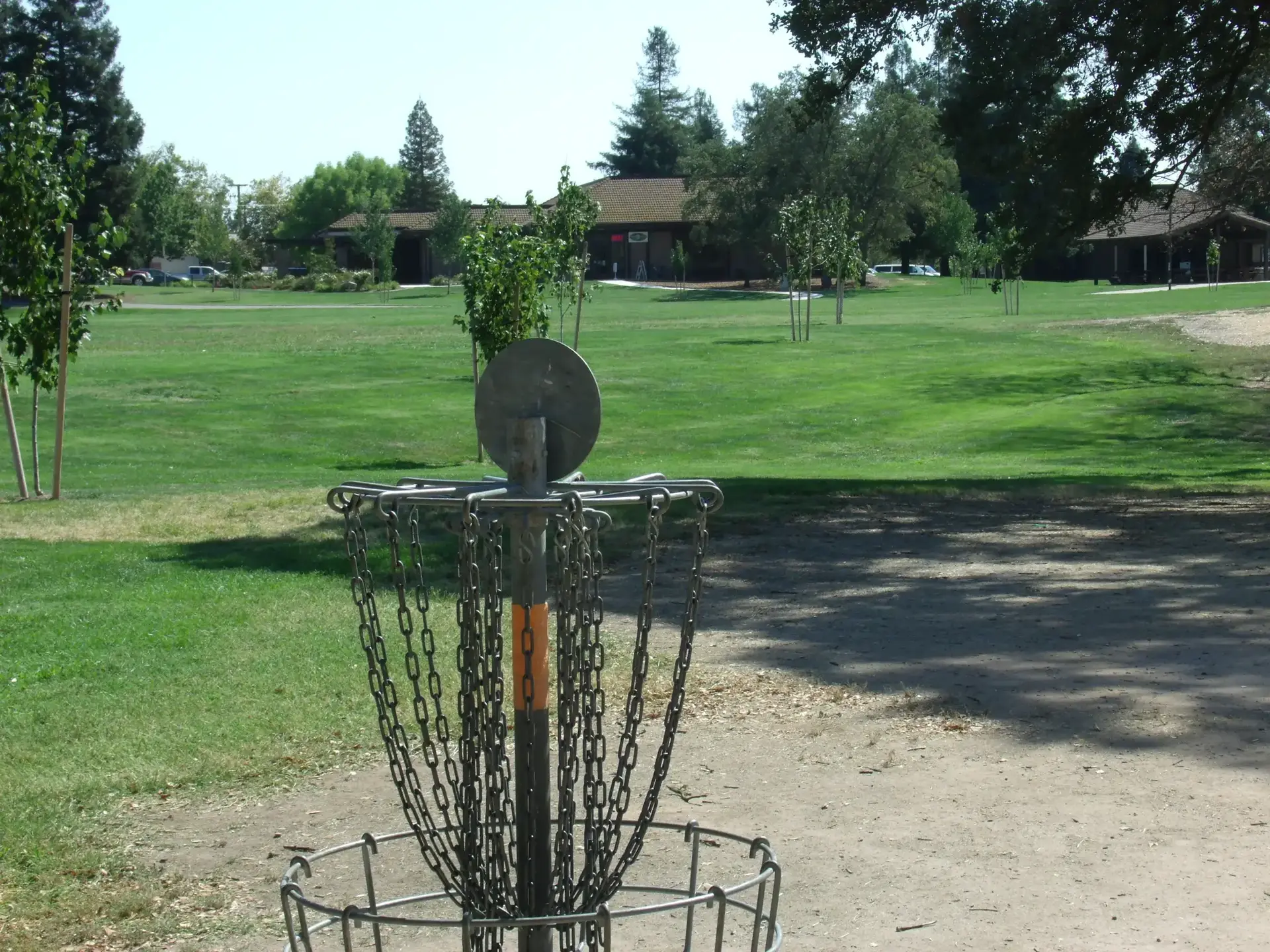 A disc golf basket stands on a sunny green course.