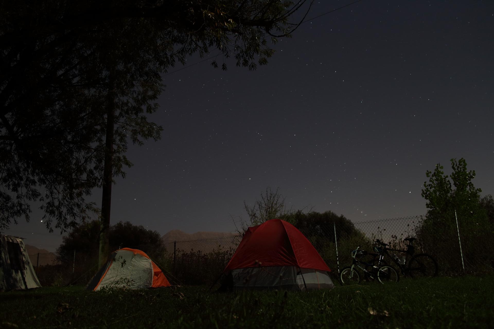 Two tents and bicycles under a dark, star-filled night sky.