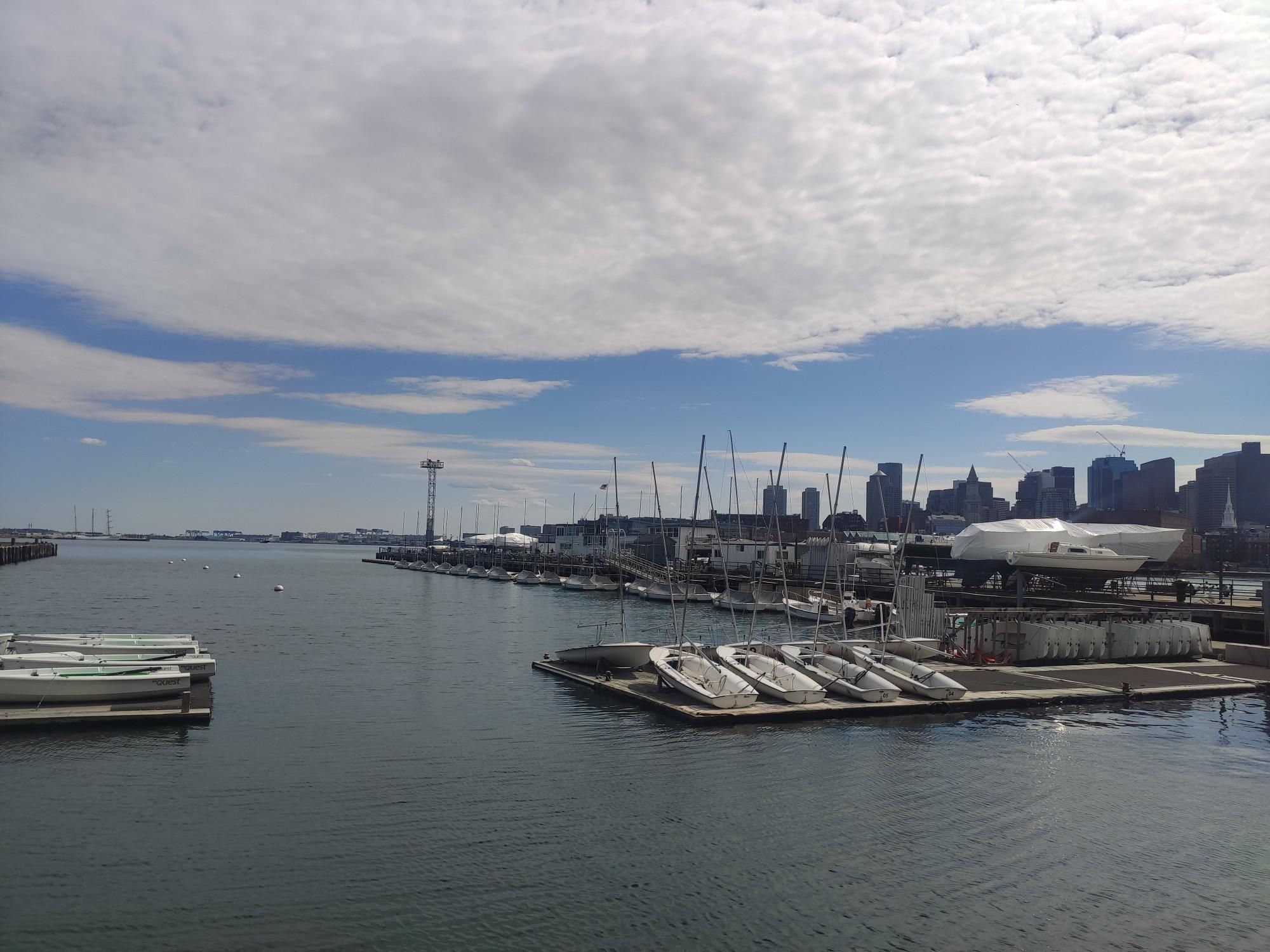 Marina filled with boats, a distant city skyline under a bright sky. - USS Constitution loop from Chelsea