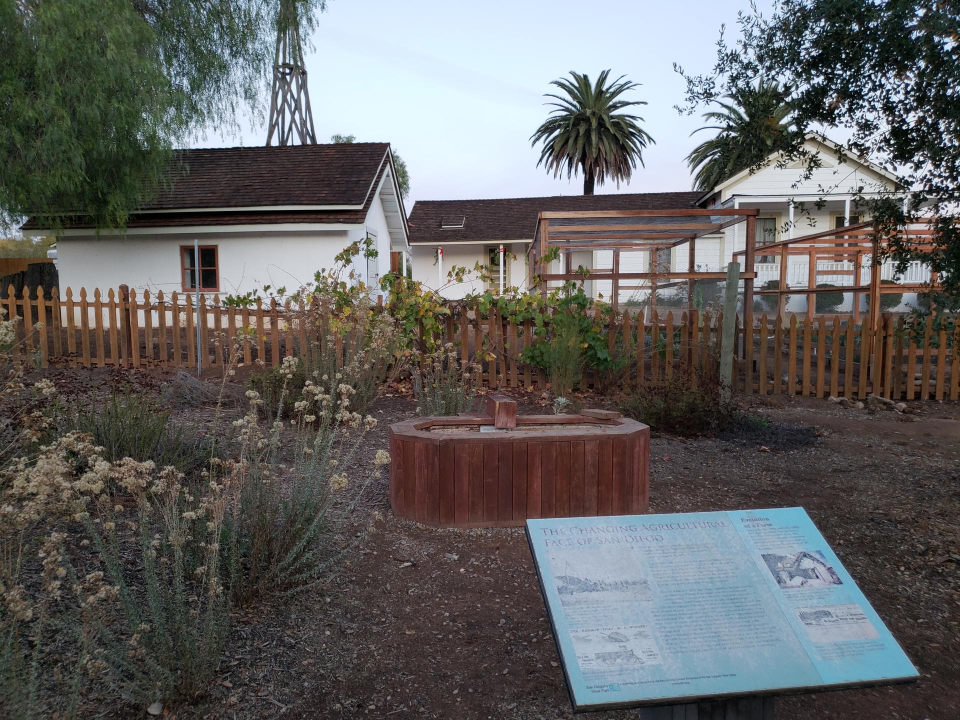 Historic white buildings with a garden and fences under an overcast sky.