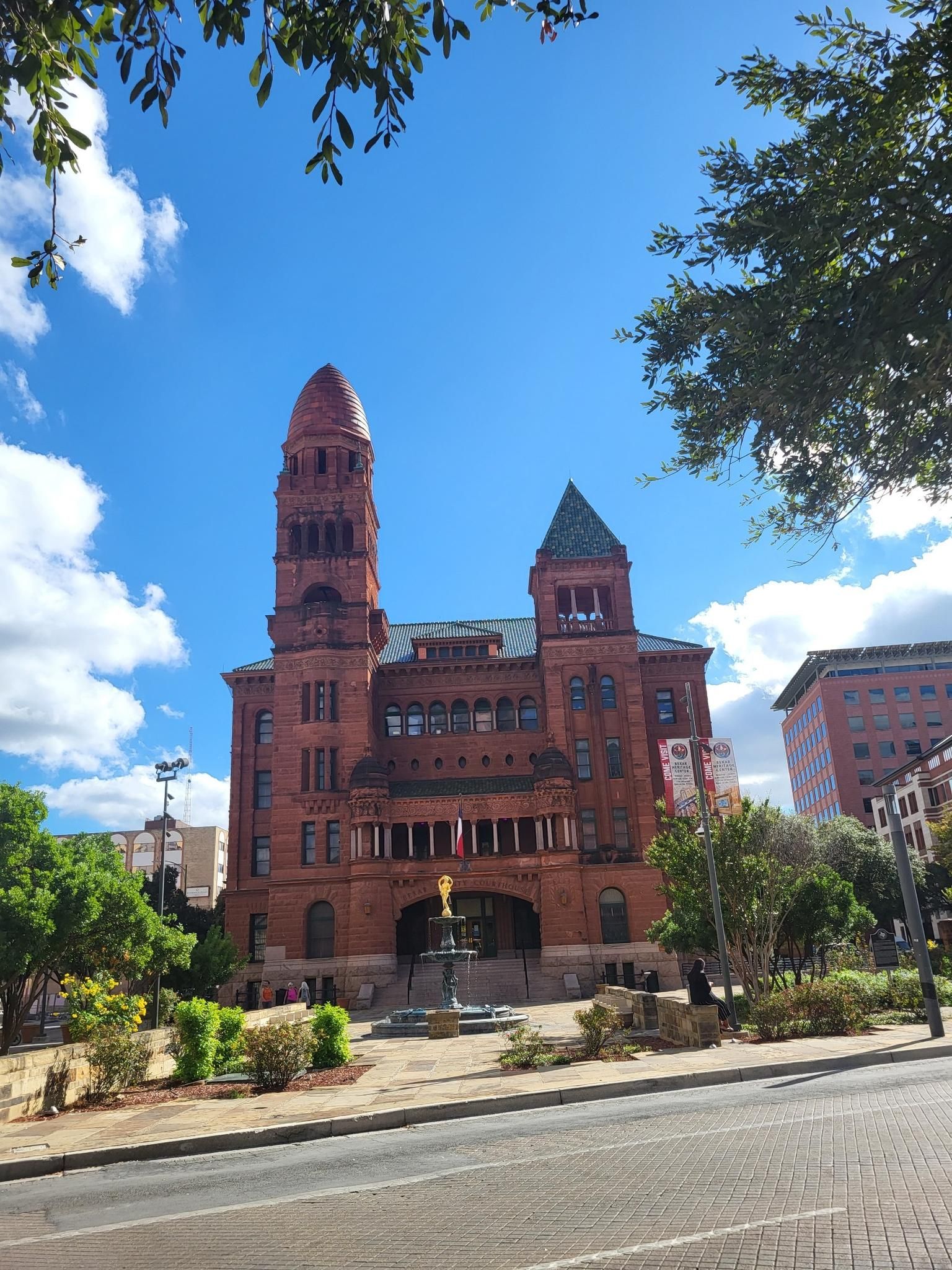 Grand red brick building with a tall tower and fountain under blue sky. - Bexar County Courthouse – San Antonio River Walk loop from San Antonio