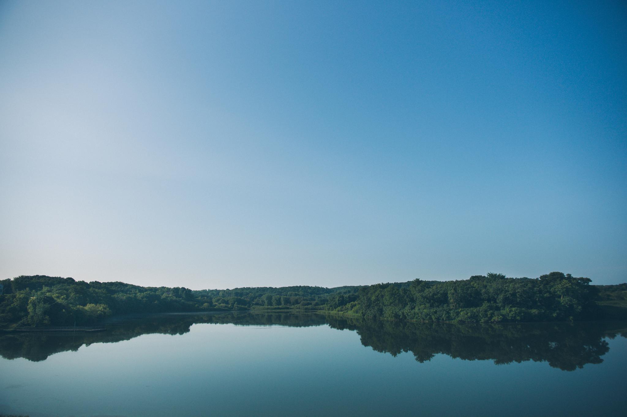 A tranquil lake perfectly reflecting a clear blue sky and distant green trees.
