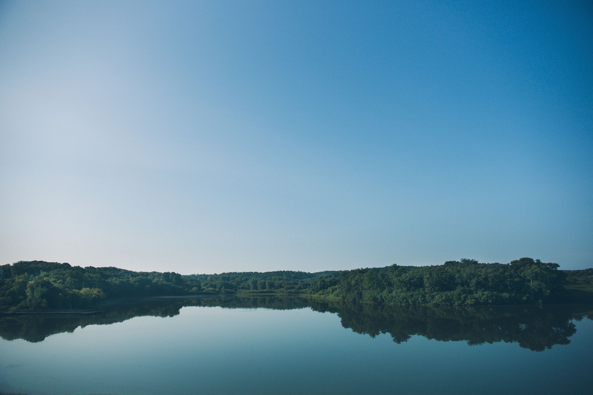 A tranquil lake perfectly reflecting a clear blue sky and distant green trees. - Willow Creek Reservoir Loop