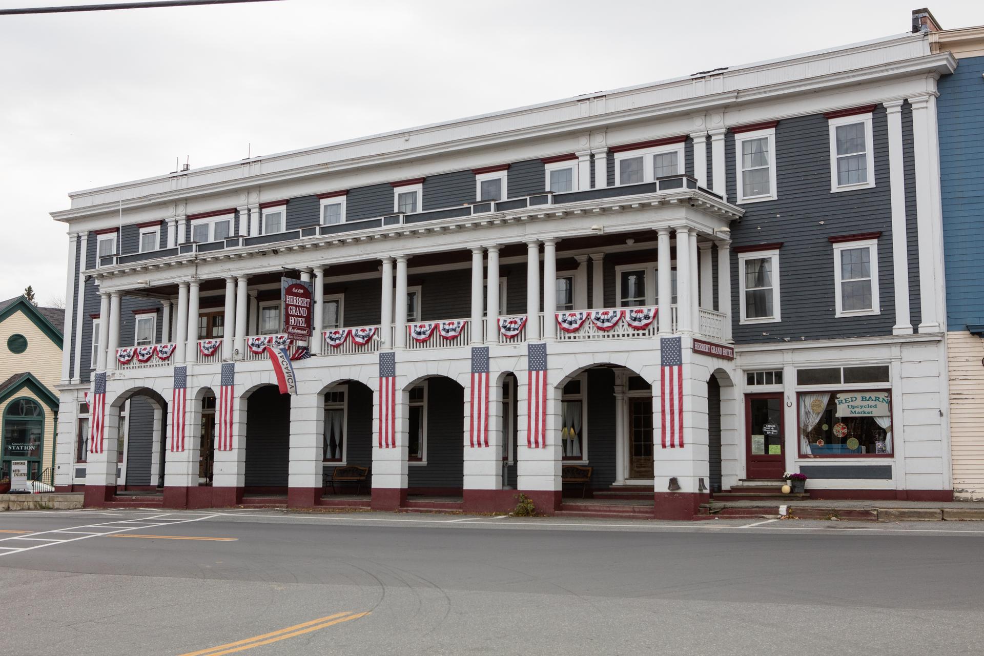 Large historic building with patriotic bunting on a two-story porch, overcast day.