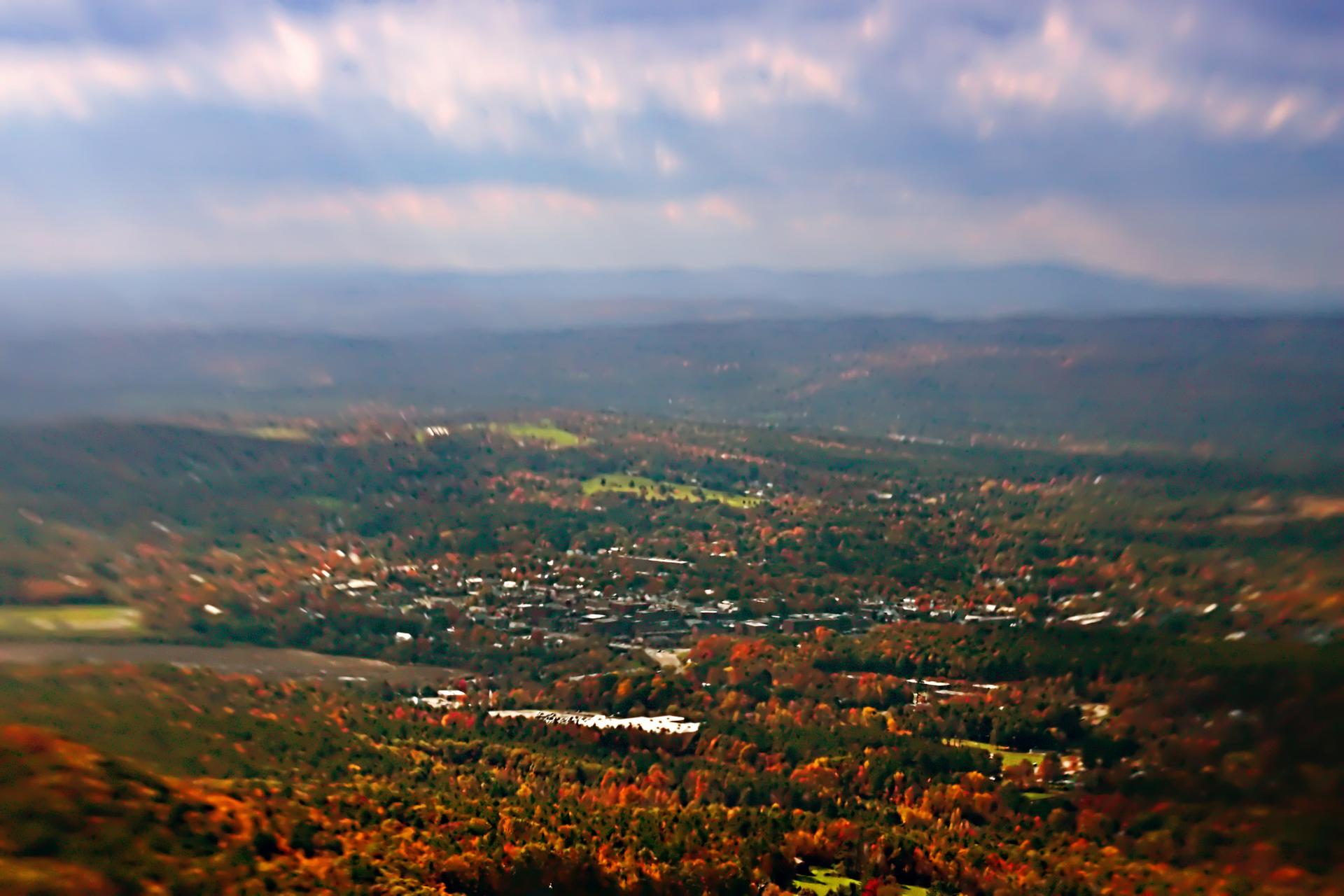 Aerial view of a town in a valley with vibrant autumn trees under cloudy skies.