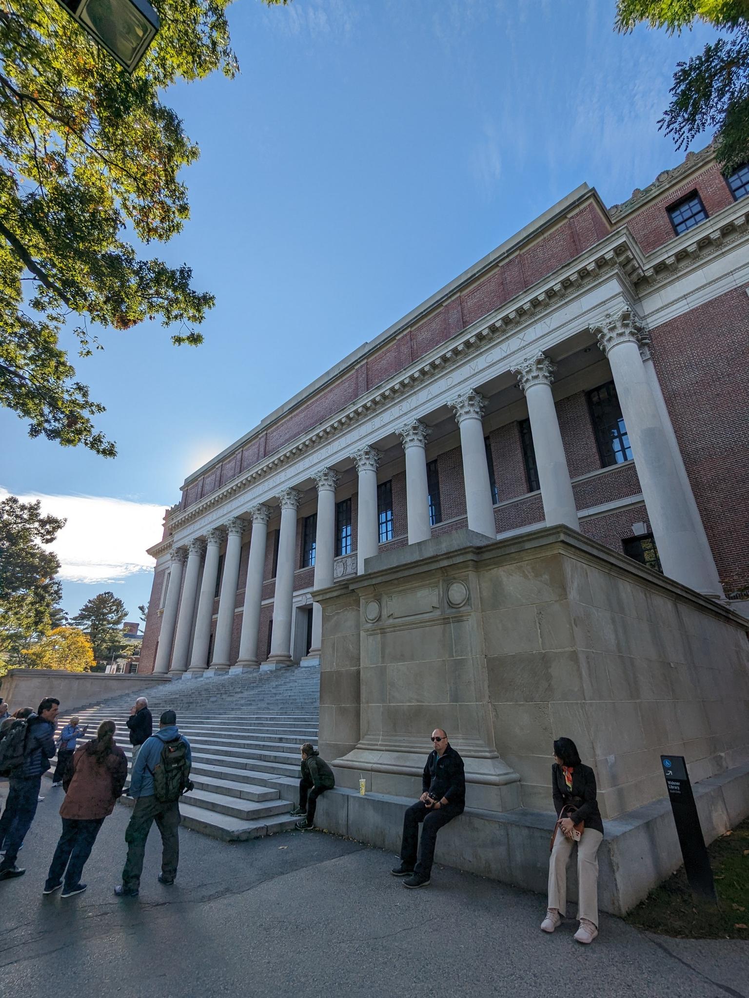 People walk and sit on steps of a grand building with columns.
