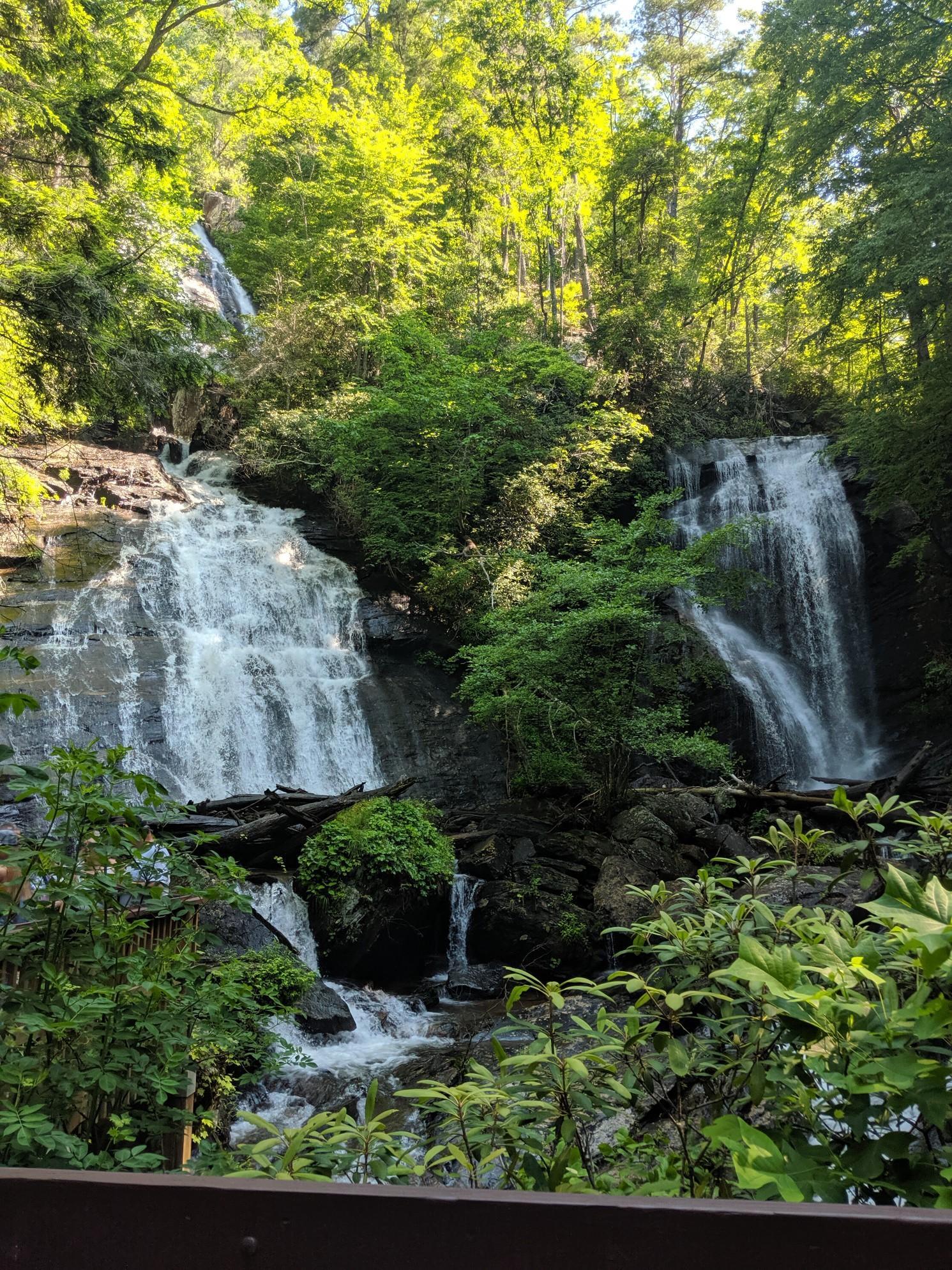 Two waterfalls flow through a lush green forest on a bright day.